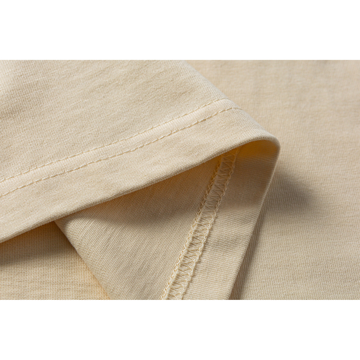 Close-up of the pale yellow T-shirt’s folded sleeve hem and overlocked seam.
