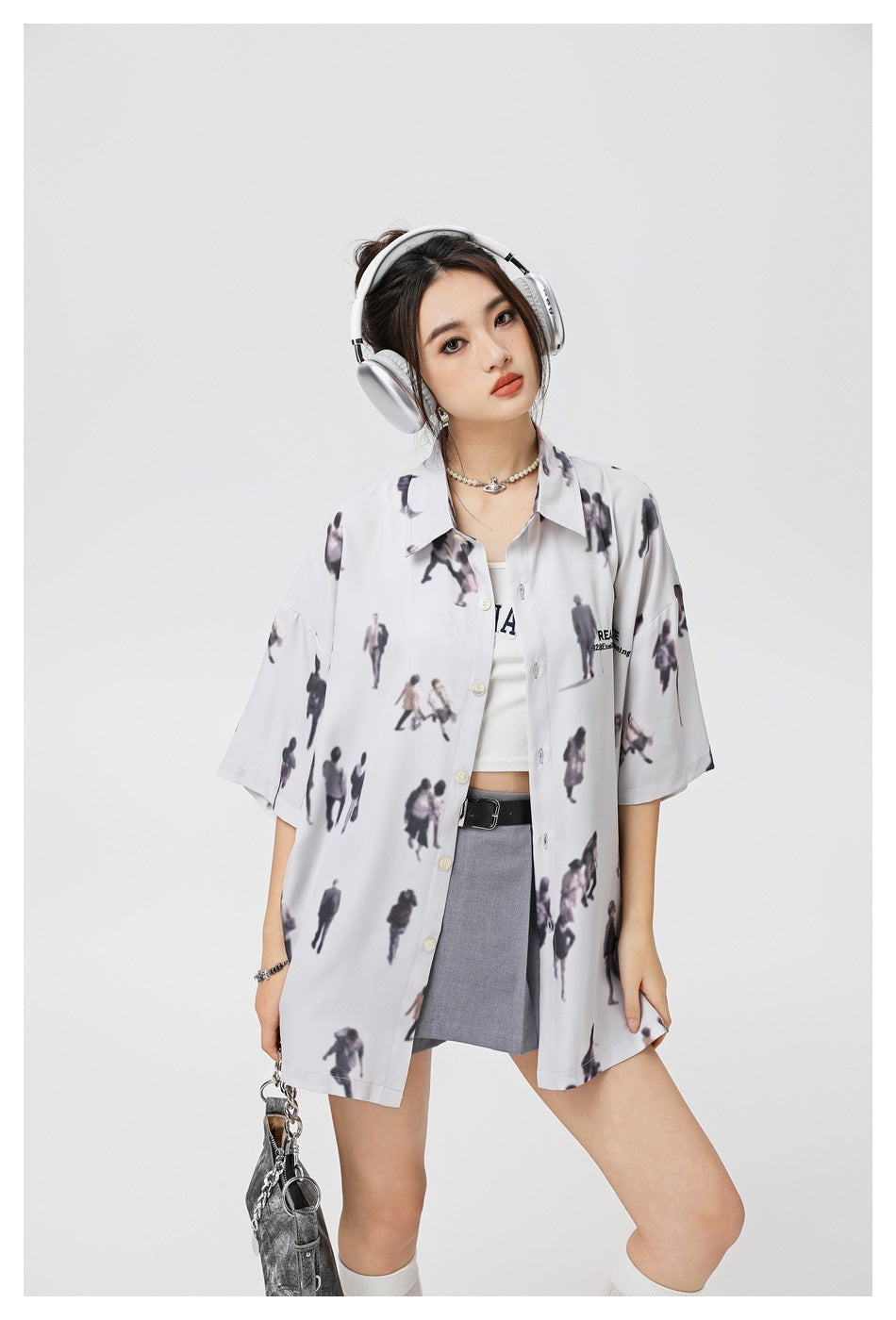 Closer view of a model wearing an oversized pale gray shirt with a scattered miniature-people print.
