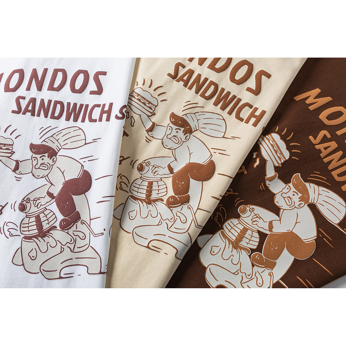 Close-up of the same illustrated sandwich-shop print on white, cream, and dark brown T-shirts.