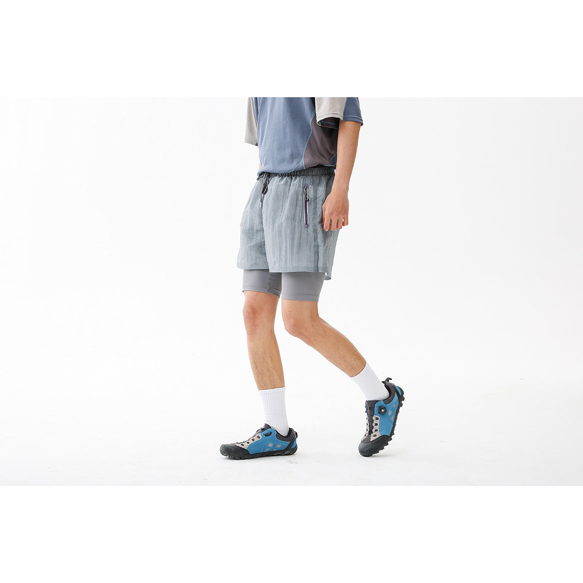 Side view of a person wearing light gray-blue running shorts over gray compression shorts, with a zip pocket visible.