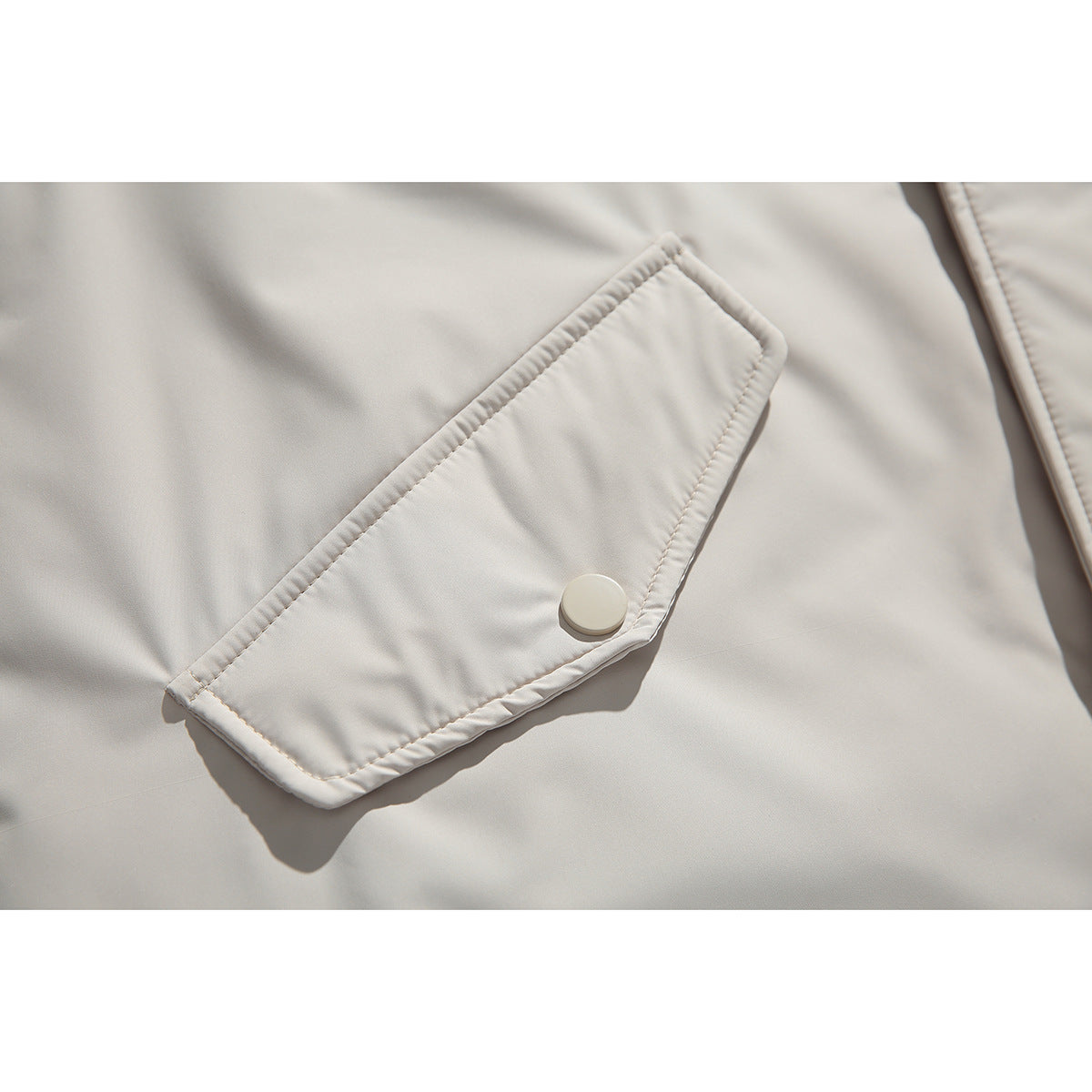 Close-up of a light beige parka's stitched pocket flap and round snap button.