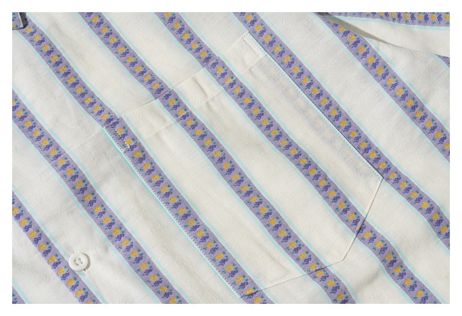 Close-up of an ivory striped shirt with lavender floral bands, turquoise edging, a white button, and a chest pocket.
