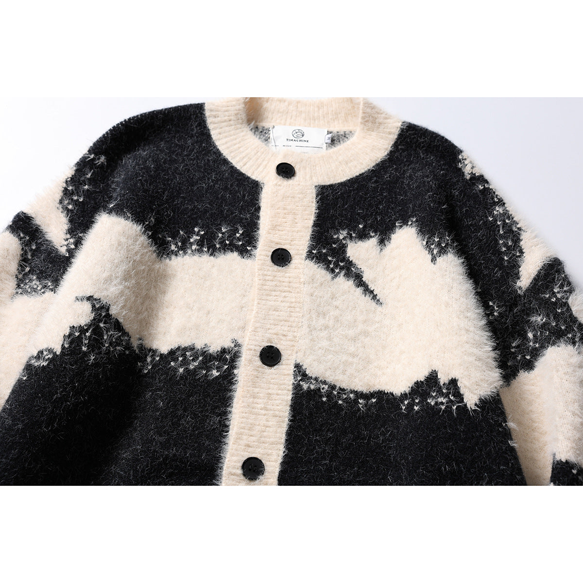 Close-up of a black and ivory fuzzy cardigan showing its round neckline, button placket, and abstract color pattern.