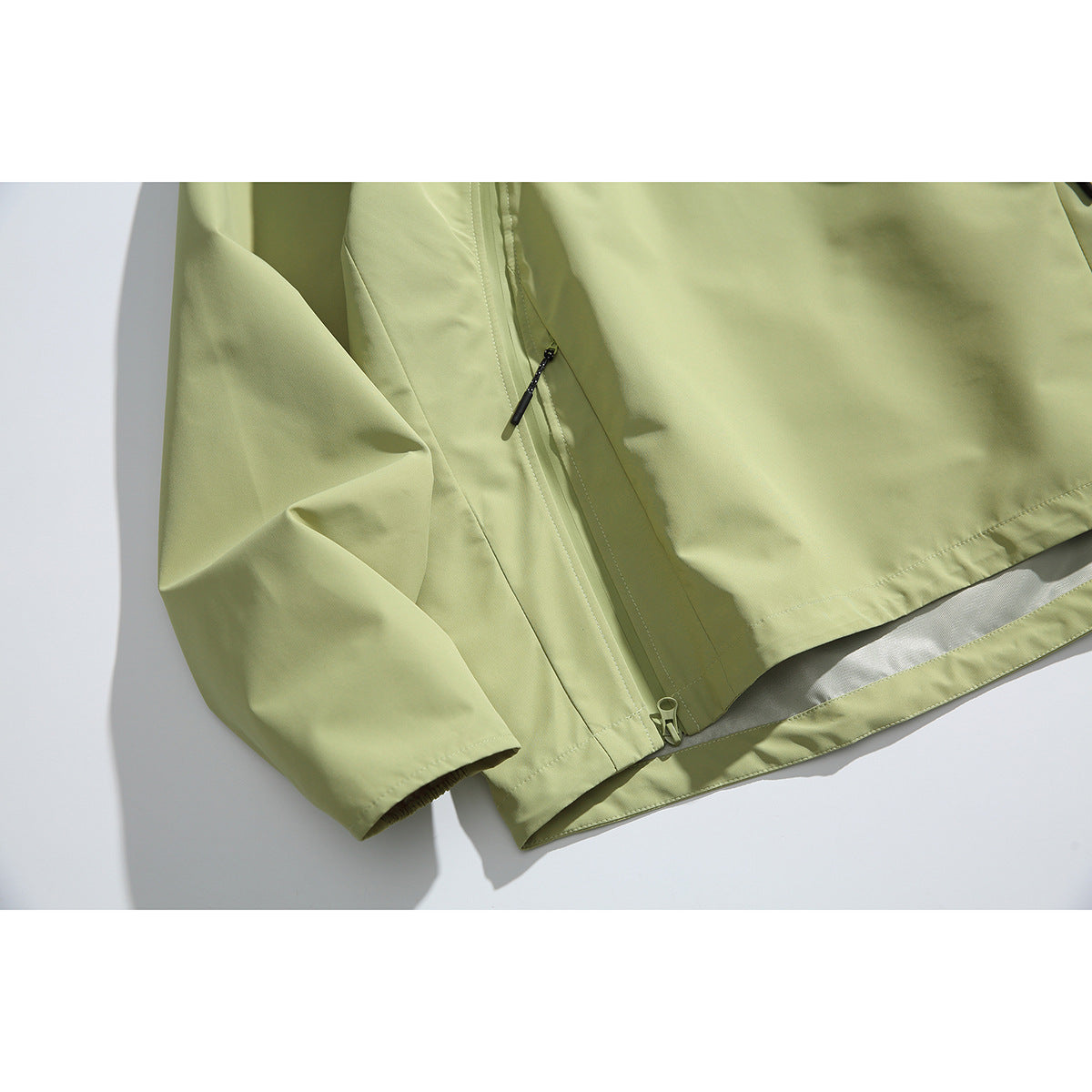 Close-up of the pale green jacket's sleeve, lower zipper, hem and stitching.
