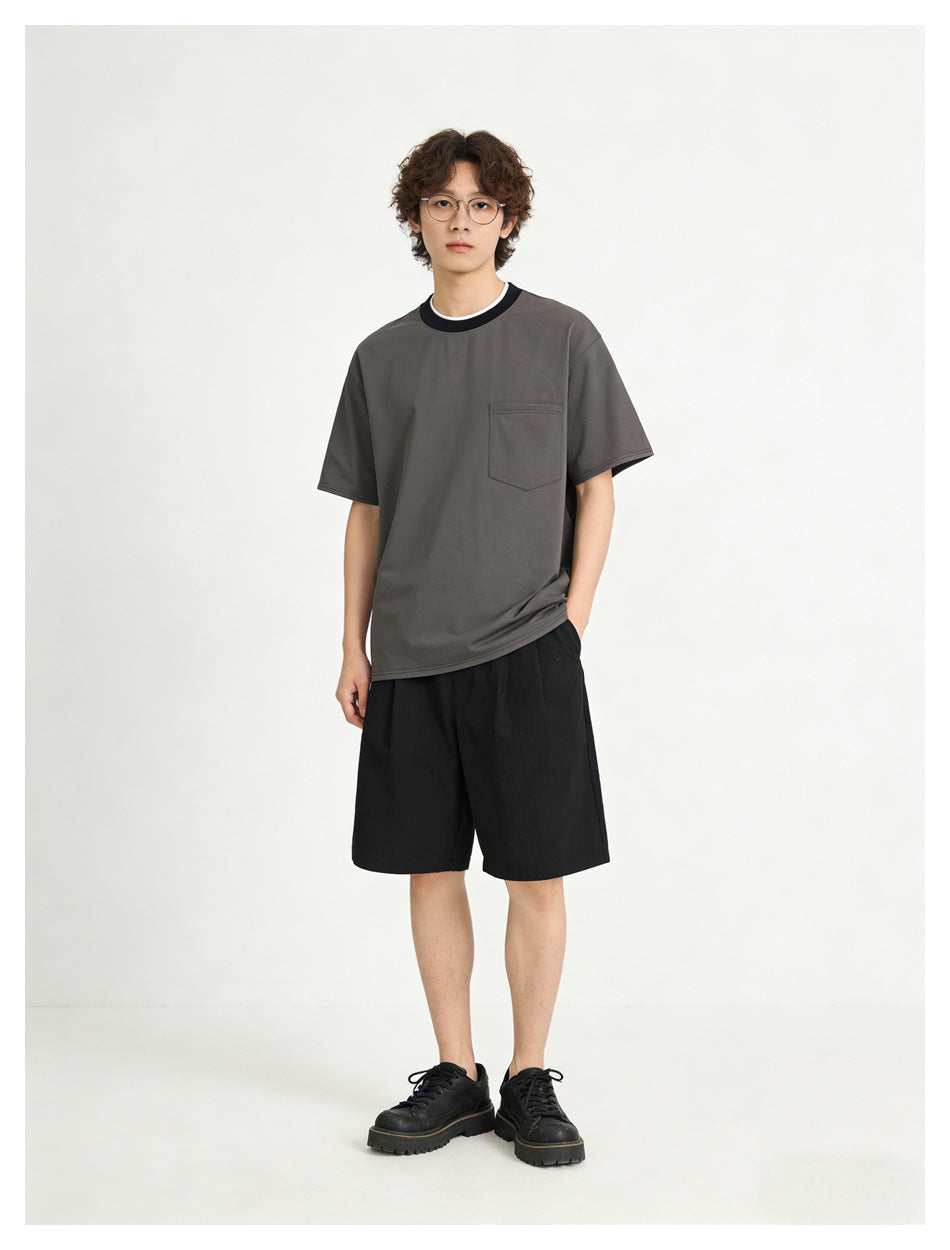 Model wearing a charcoal short-sleeve T-shirt with a chest pocket and dark contrast collar, paired with black shorts.