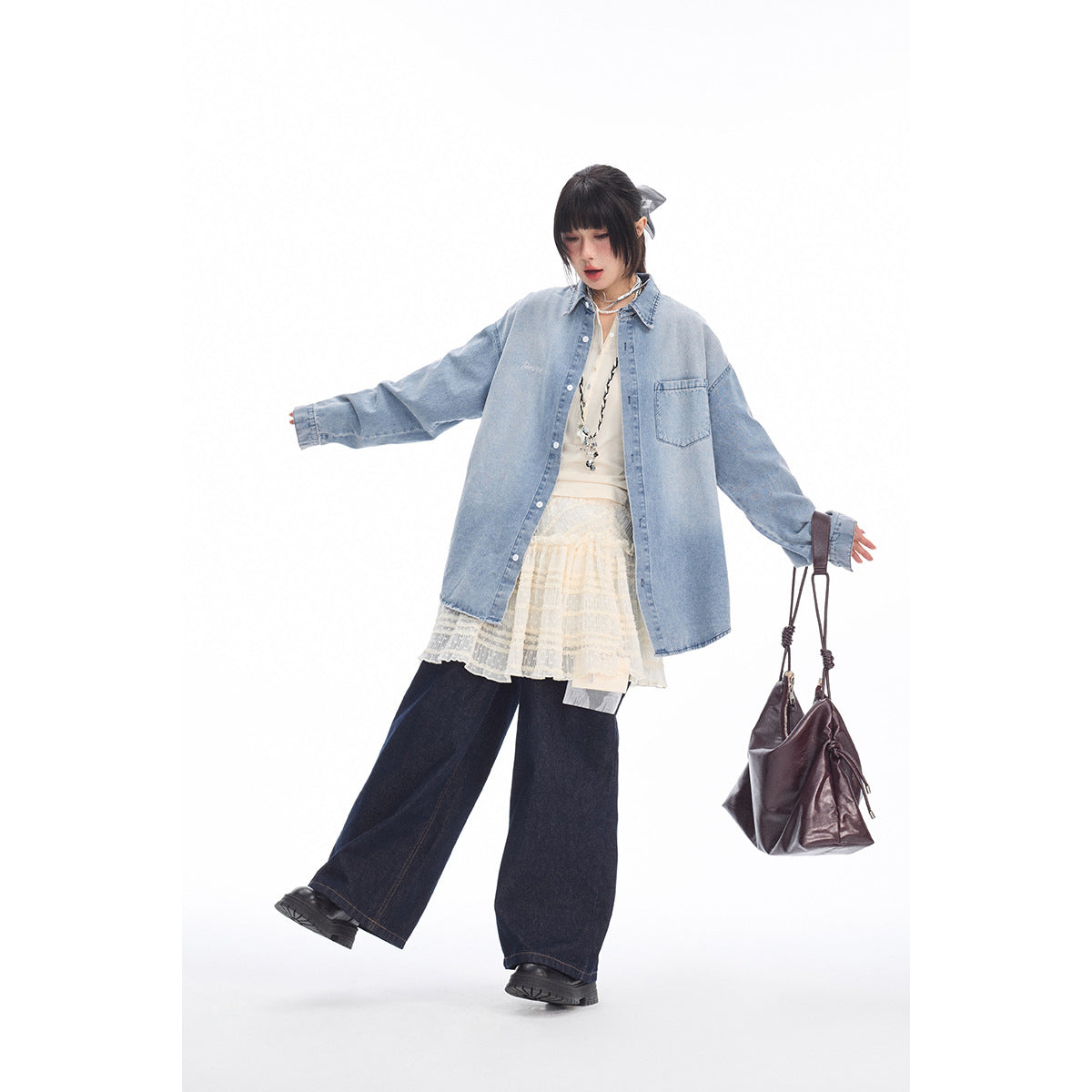 Full-length model wears an oversized light blue denim shirt over a cream lace skirt and top with dark wide-leg jeans.