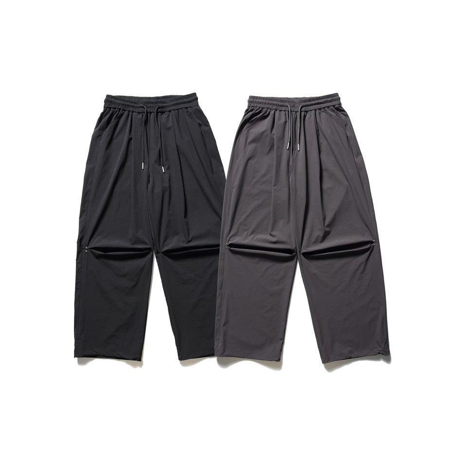 Two pairs of loose drawstring trousers laid flat, one black and one dark gray.