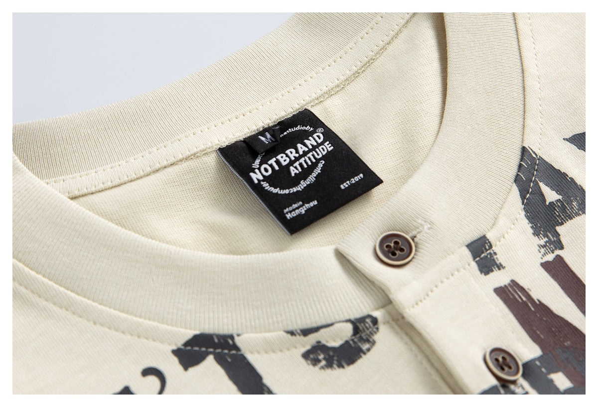 Close-up of a cream henley shirt's collar, two brown buttons, printed lettering, and black neck label.