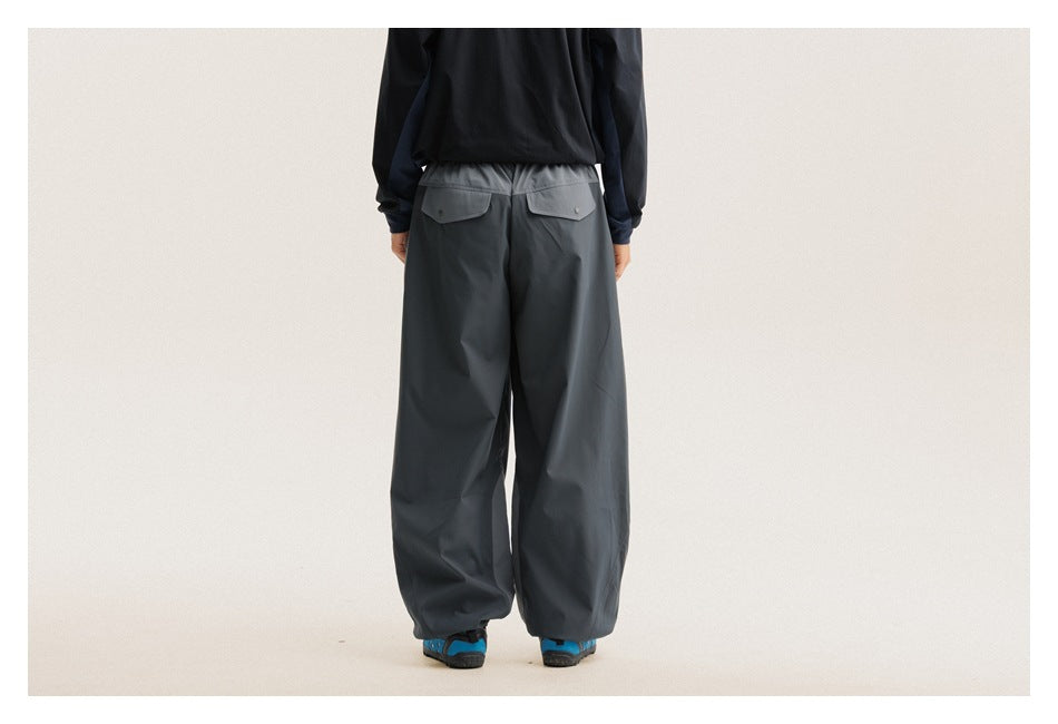 Back view of loose charcoal-gray pants with two button-flap pockets and gathered ankles, worn by a model.