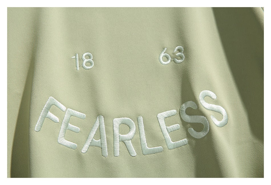 White embroidered “18,” “63,” and “FEARLESS” lettering on pale sage-green sweatshirt fabric.