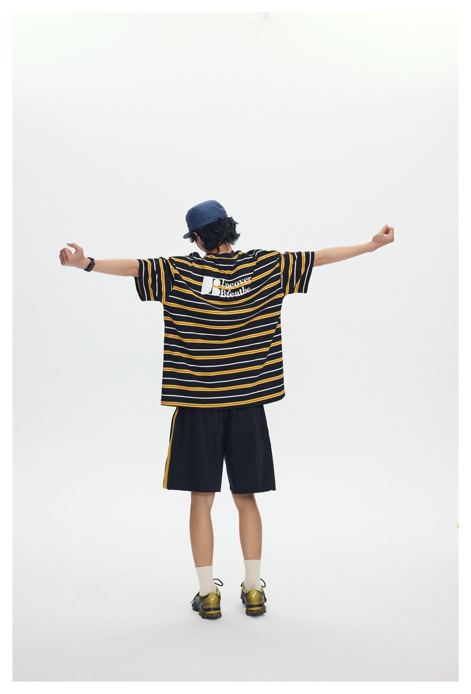 Model with arms outstretched seen from behind in a yellow-striped T-shirt with Uncover Breathe print