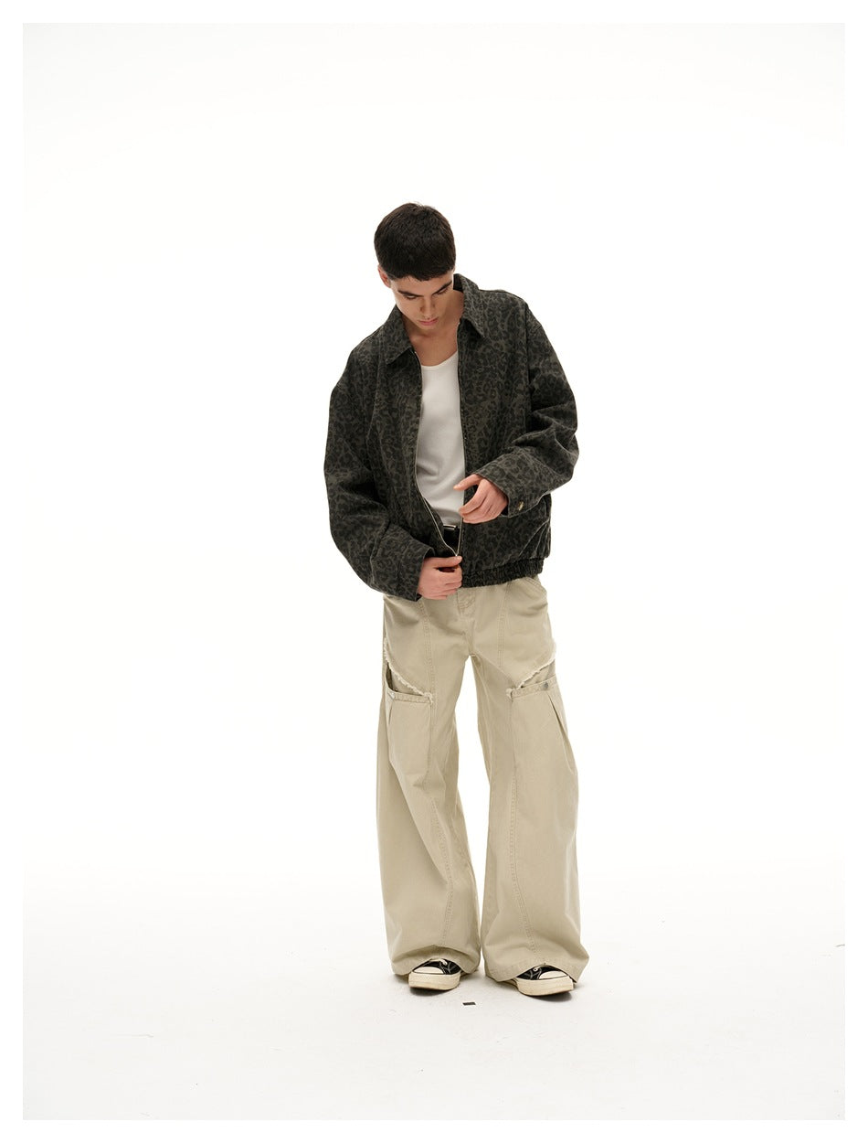 Model looking down while adjusting a dark olive leopard-print jacket over a white top and beige trousers.