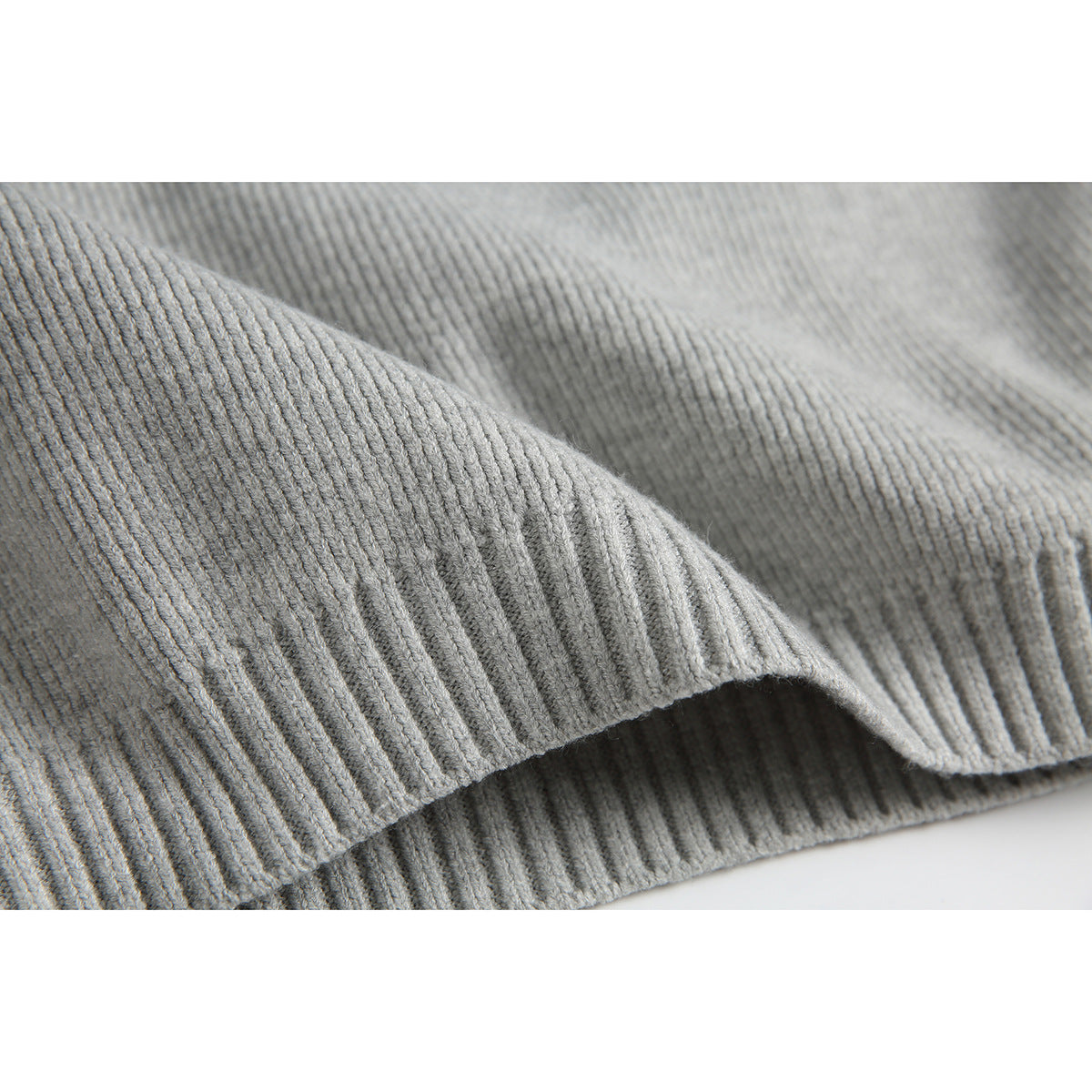 Close-up of the light gray sweater’s ribbed knit fabric and folded hem edge.