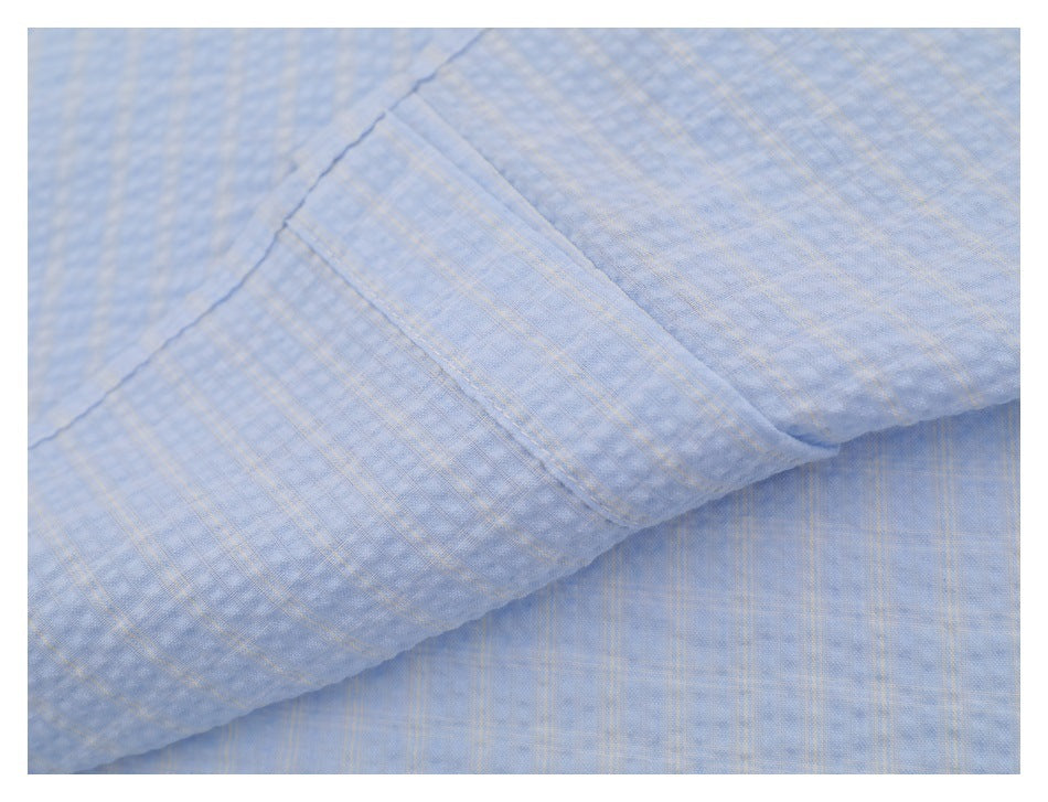 Close-up of a folded, stitched edge on light blue subtly checked shirt fabric.