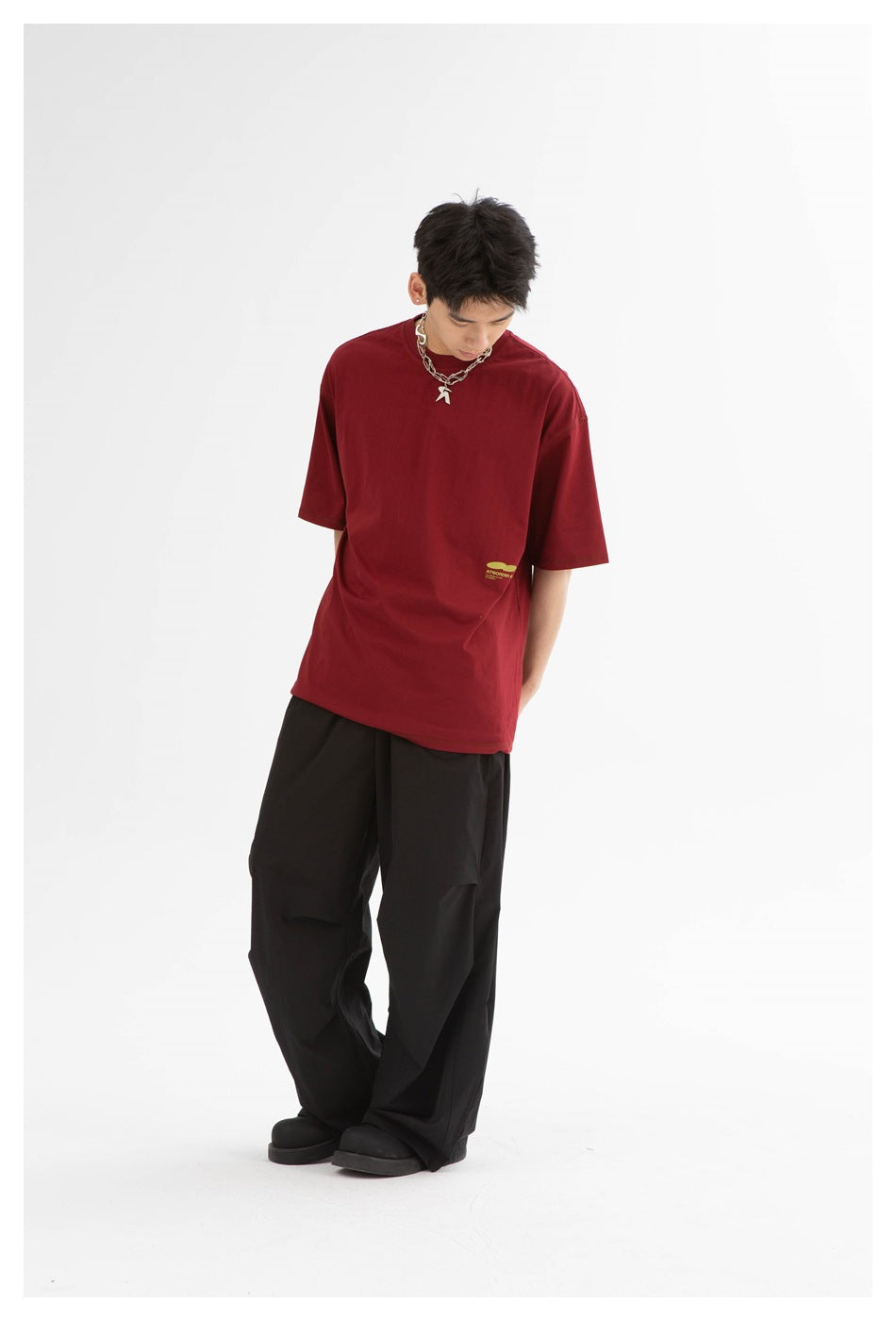 Model wearing a burgundy oversized T-shirt, front view, with a small yellow logo near the hem.