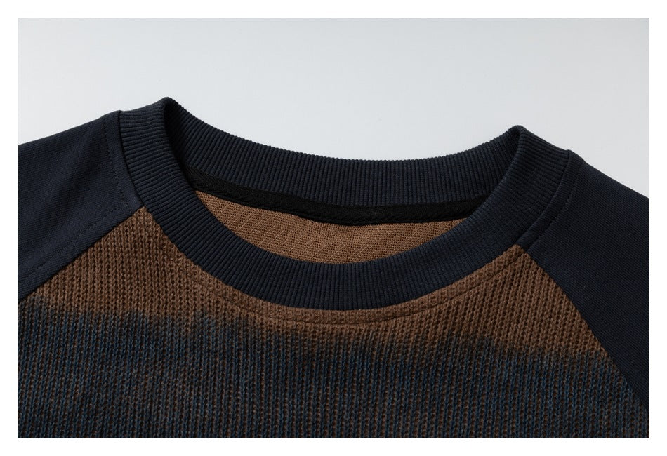 Close-up of a dark ribbed crew neckline, navy raglan shoulders, and brown-and-blue textured knit.