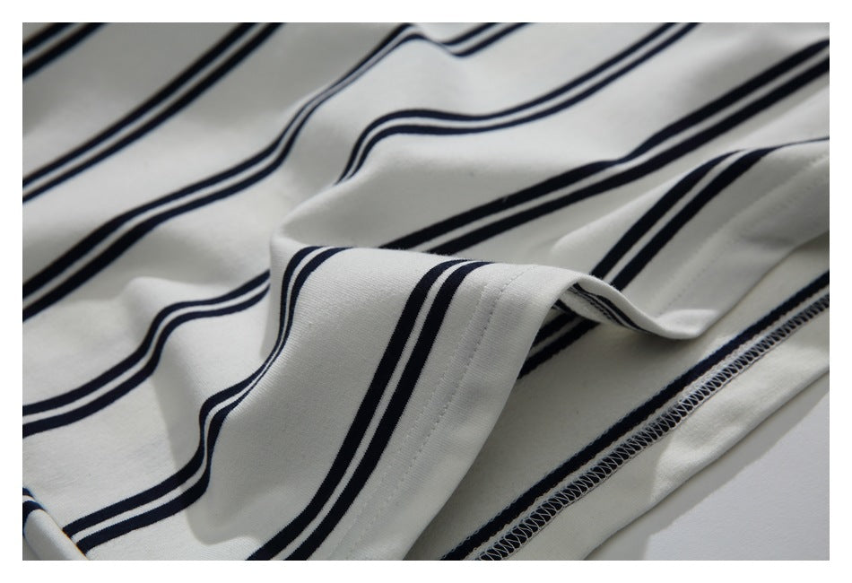 Close-up of cream fabric with navy stripes, folded to show a stitched hem and overlocked seam.