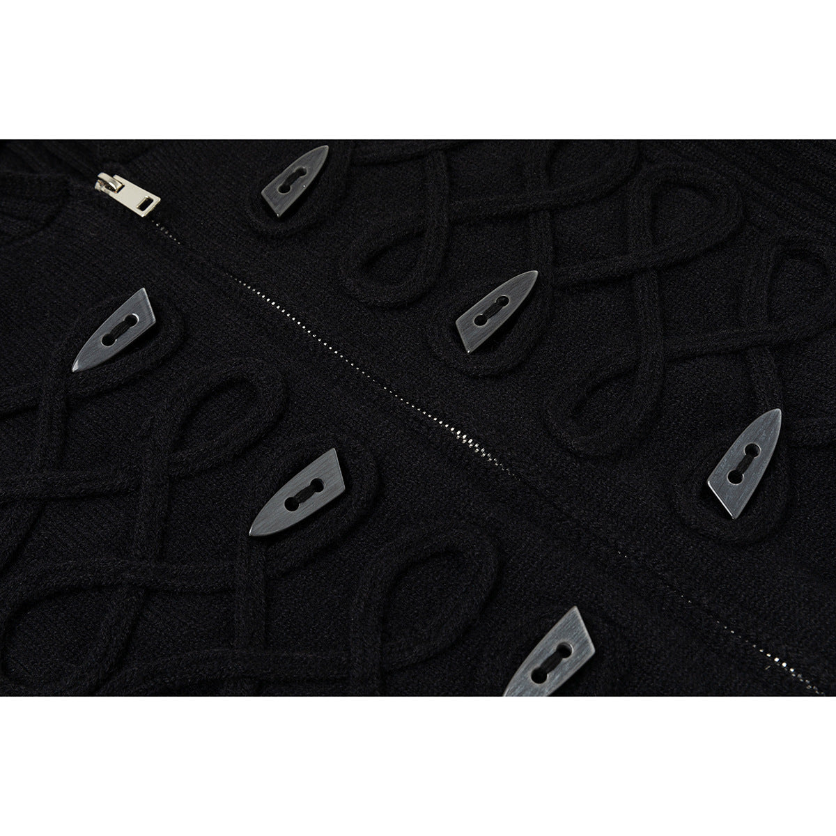 Close-up of a black cardigan’s raised knit pattern, silver zipper, and dark toggle buttons.