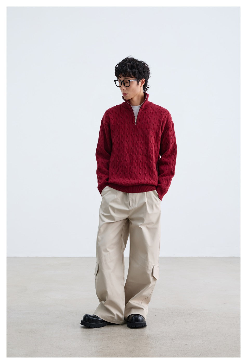 Front view of a model wearing a burgundy cable-knit quarter-zip sweater with a raised collar and wide beige trousers.