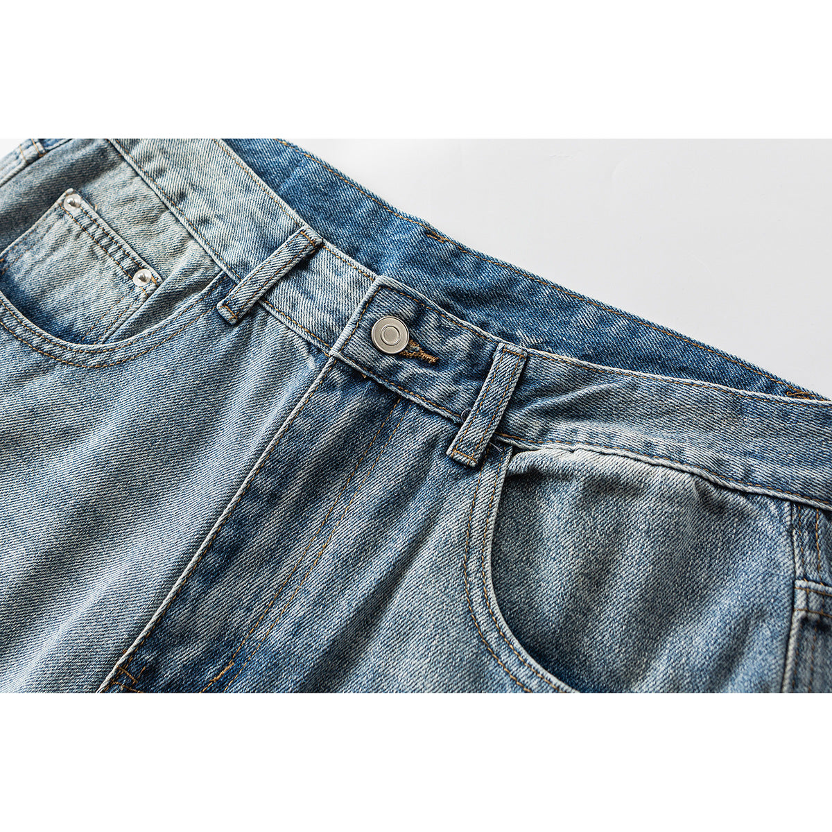 Close-up of faded blue jeans showing the waistband, metal button, belt loops, fly and front pocket.