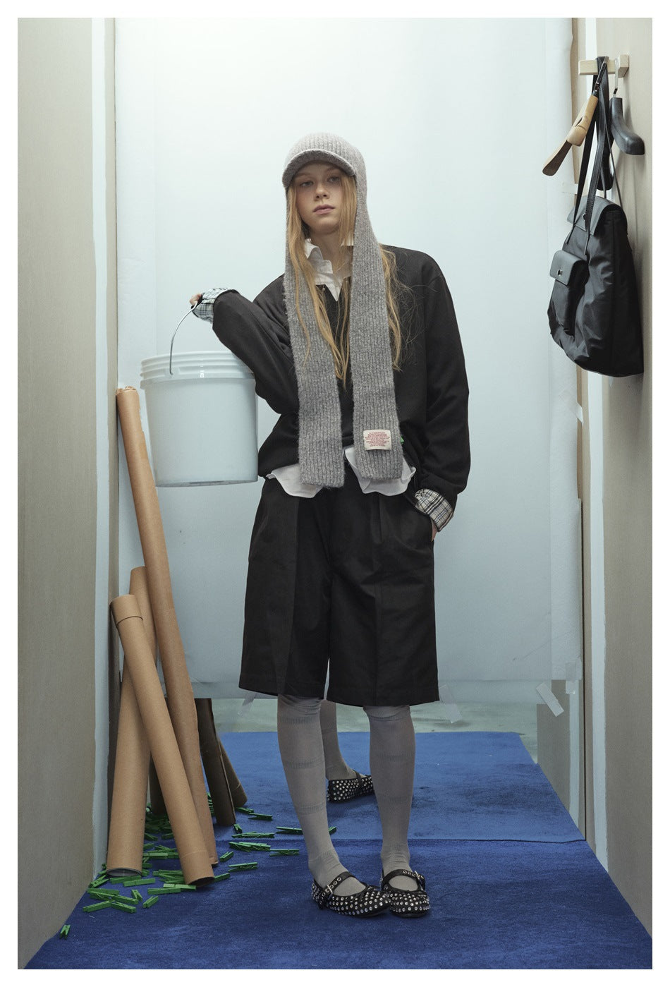 Front view of a model wearing a black long-sleeve top and knee-length shorts, white shirt, gray long scarf, and knit cap.
