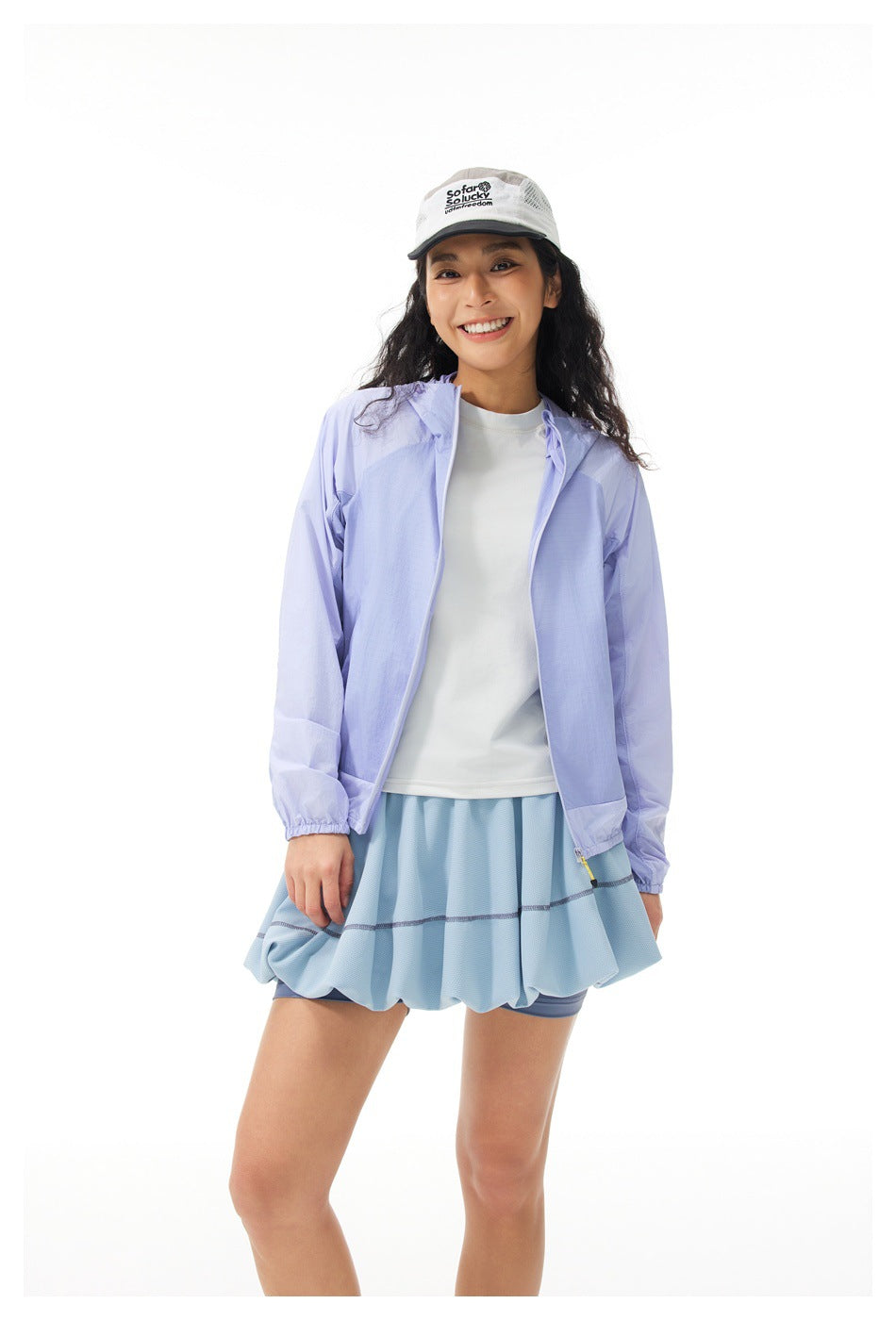 Woman wearing an open purple hooded jacket over a white tee and light blue skirt, front view, with a white cap