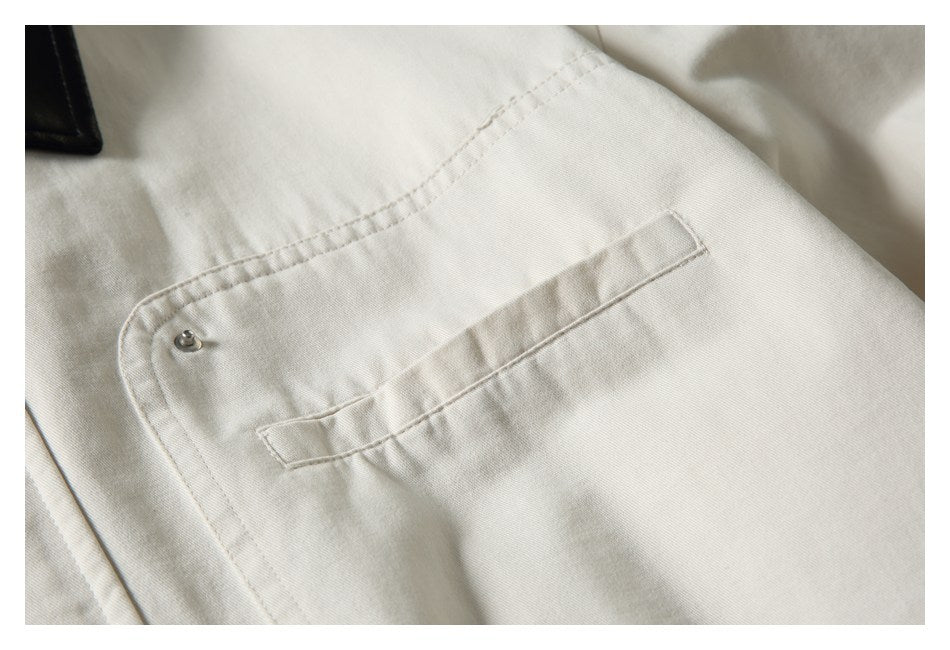 Close-up of a cream jacket pocket with a small metal snap and stitched edges.