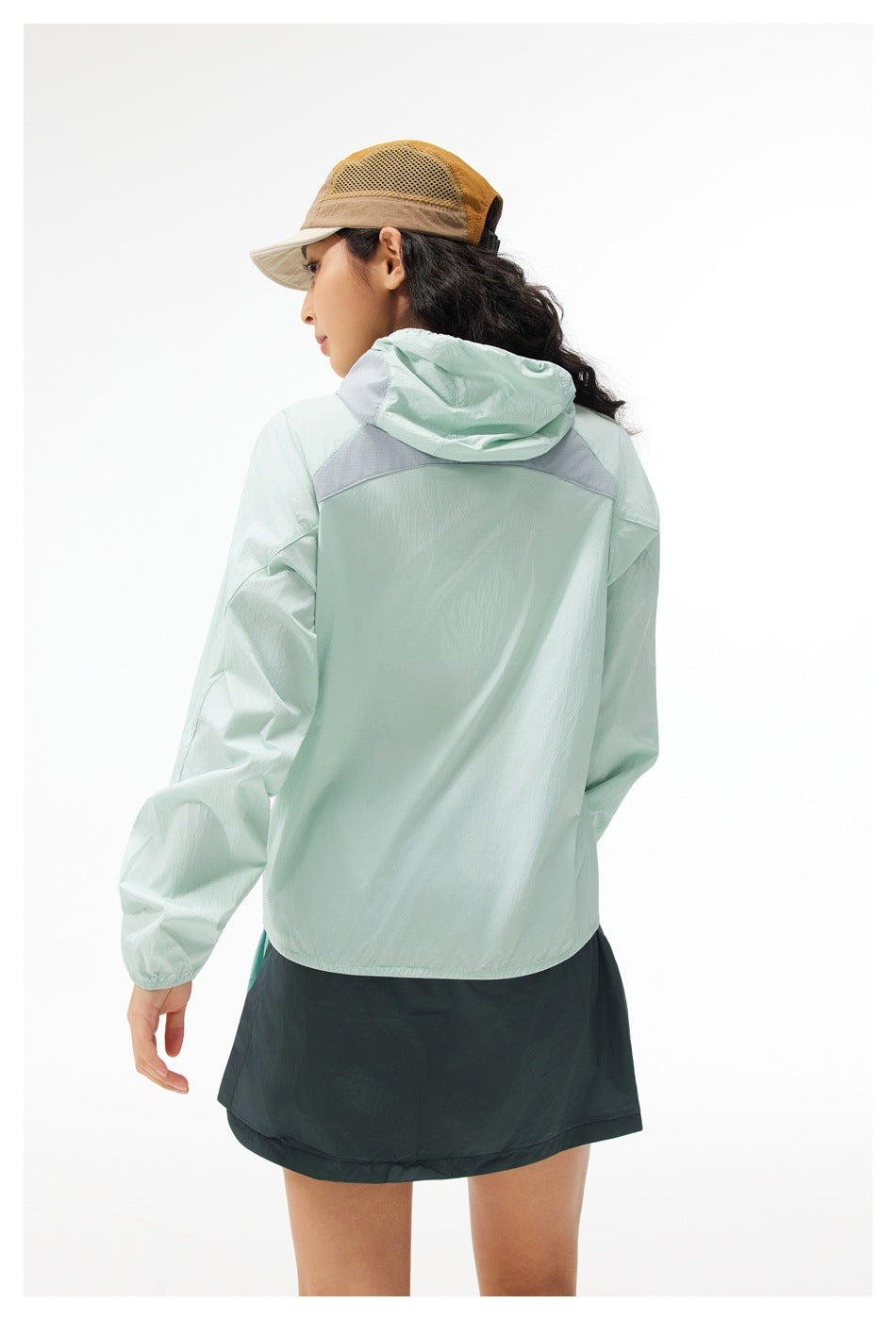 Back view of a model wearing a pale mint hooded jacket with a light gray shoulder panel and dark teal skirt.