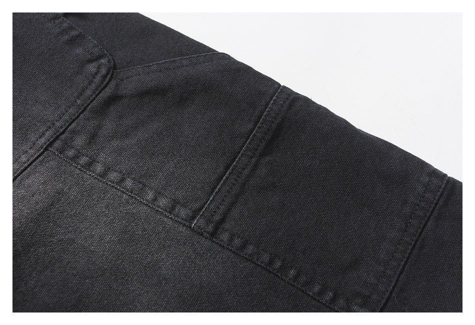 Close-up of black trouser construction showing a rectangular stitched panel and intersecting seams.