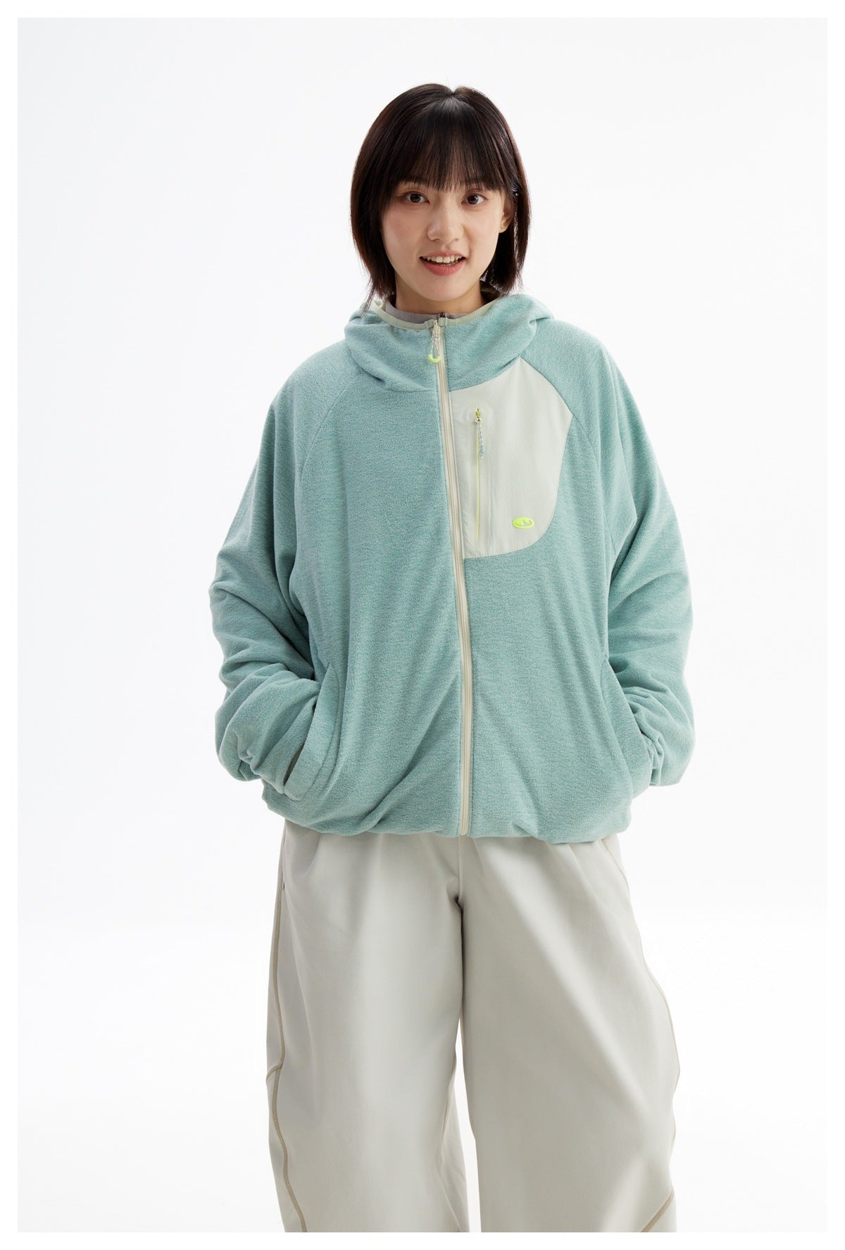 Closer view of a model wearing a mint-green hooded zip jacket with a cream chest panel and front pockets.