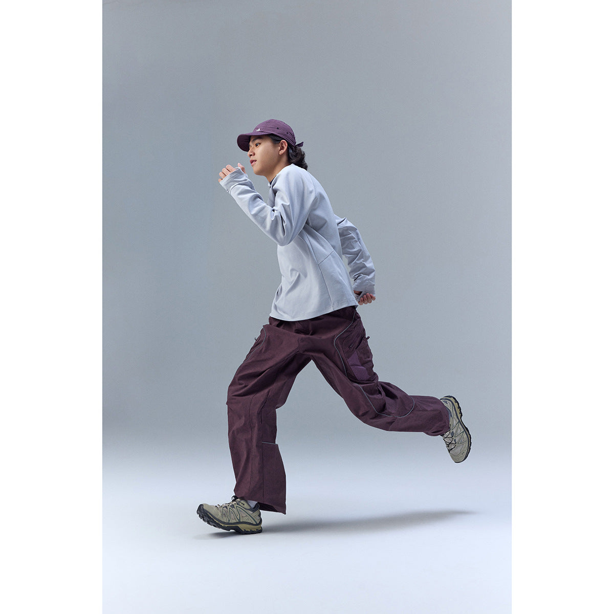 Model running in a pale blue long-sleeve top and loose plum cargo trousers with curved seam details.