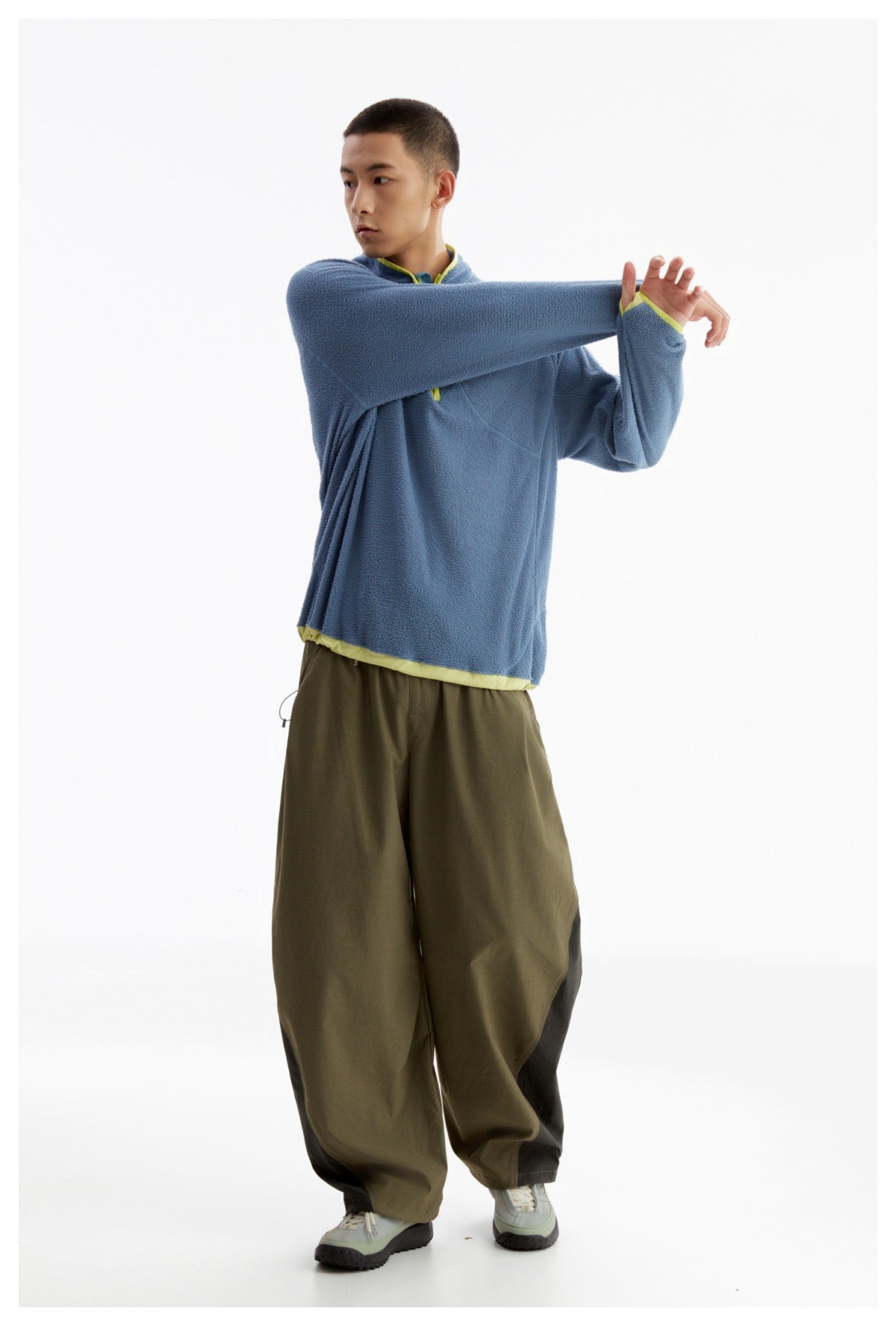Model wearing a blue fleece pullover with lime trim and loose olive pants with dark panels.