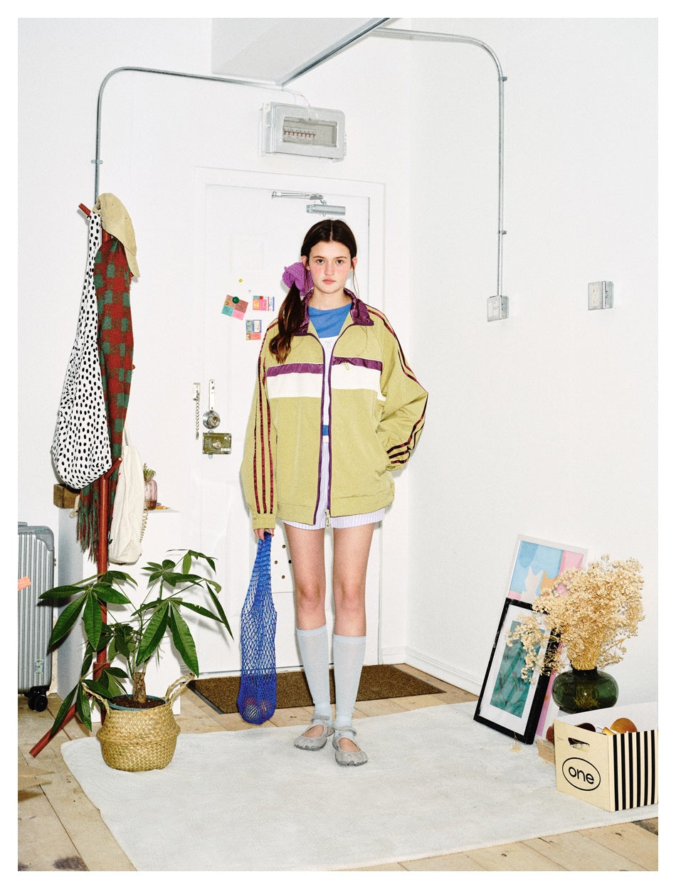 Full-length model wears a khaki track jacket with purple-and-white chest stripes and striped sleeves.