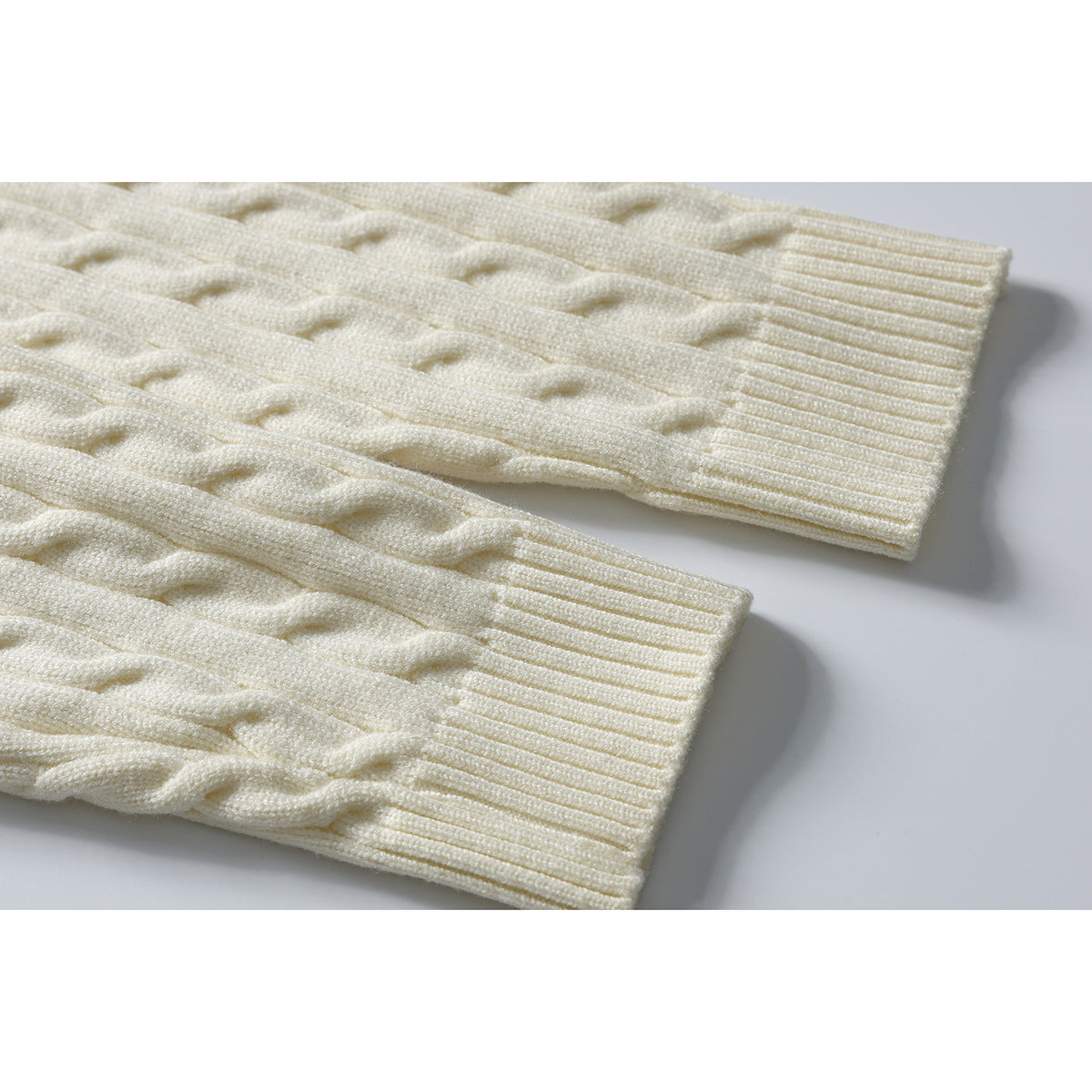 Close-up of an ivory cable-knit sweater sleeve and ribbed cuff.