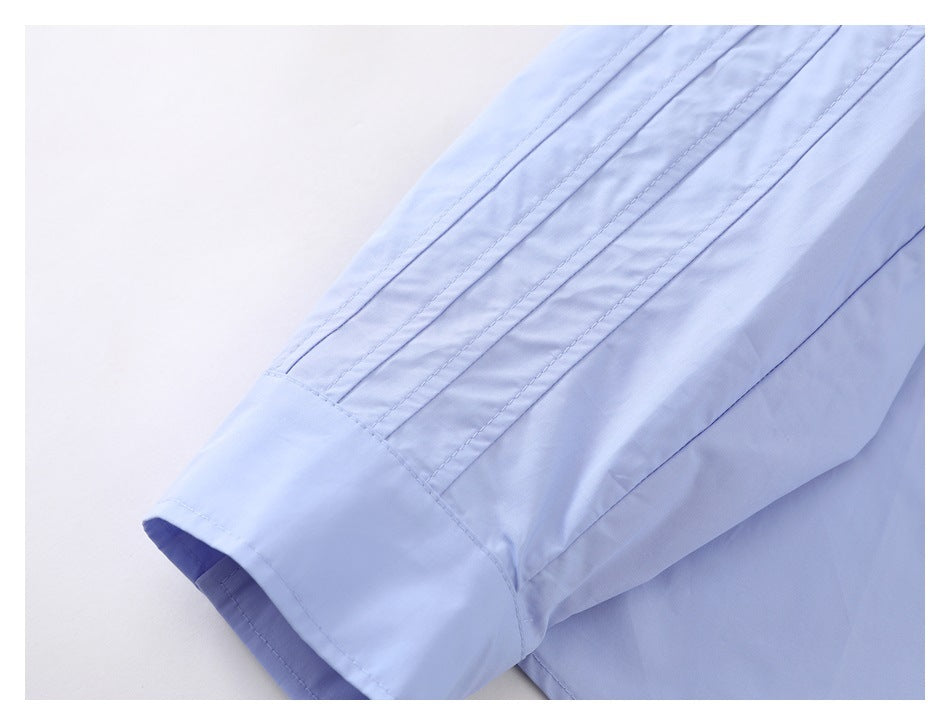 Close-up of a light blue shirt sleeve with parallel stitched pleats and a wide cuff.