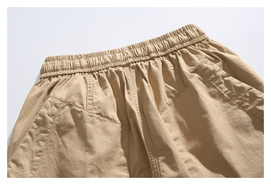 Close-up of tan shorts with an elastic waistband, front seam, and angled pocket details.