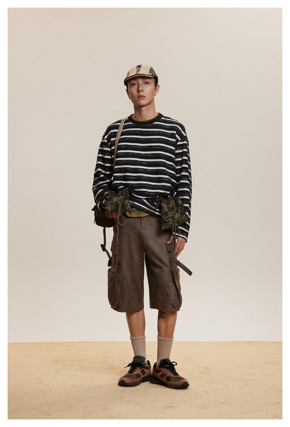 Full-length front view of a model in a black-and-cream striped long-sleeve shirt and brown cargo shorts.