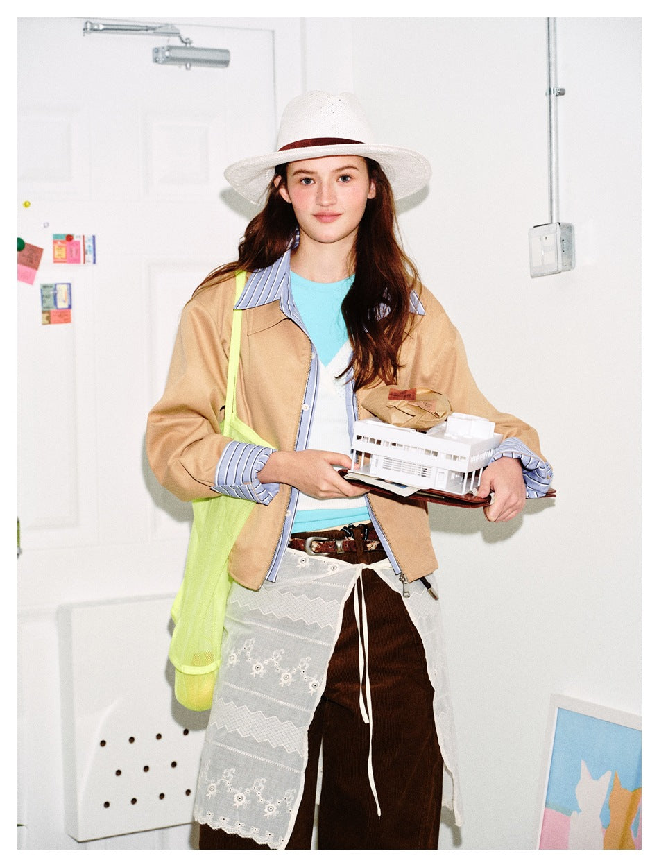Front view of a model wearing a tan jacket with blue striped collar and cuffs over a turquoise top.