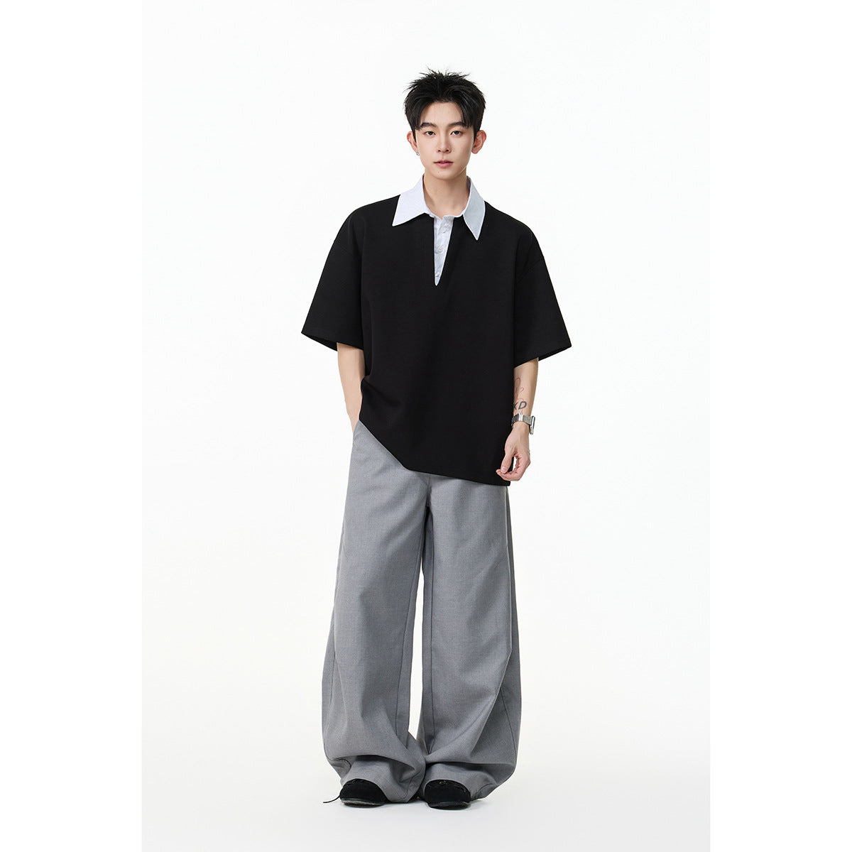 Model wearing a black oversized short-sleeve polo-style shirt with a white pointed collar and gray wide-leg trousers.