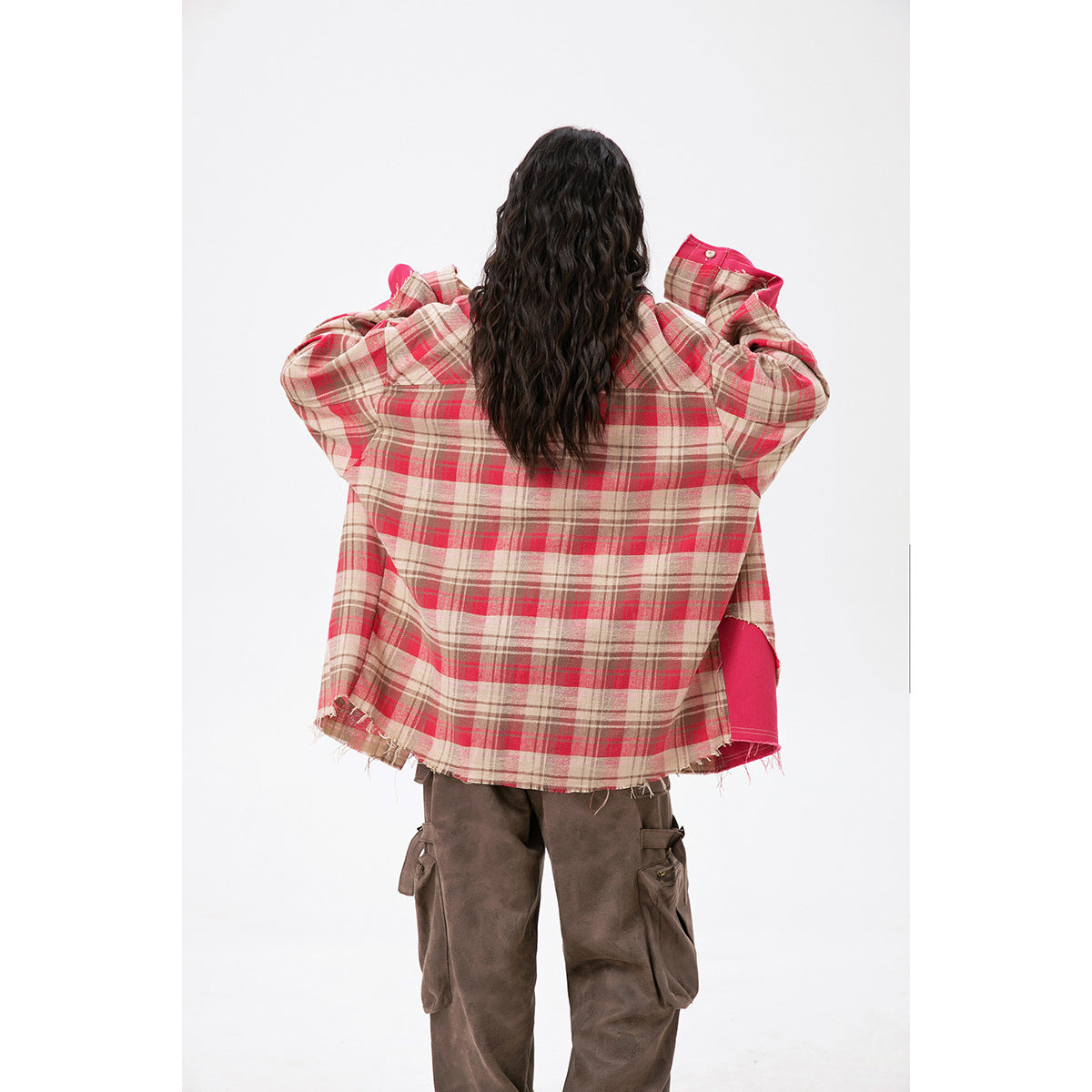 Rear view of a model wearing an oversized beige and red plaid shirt with a bright pink side panel and frayed hem.