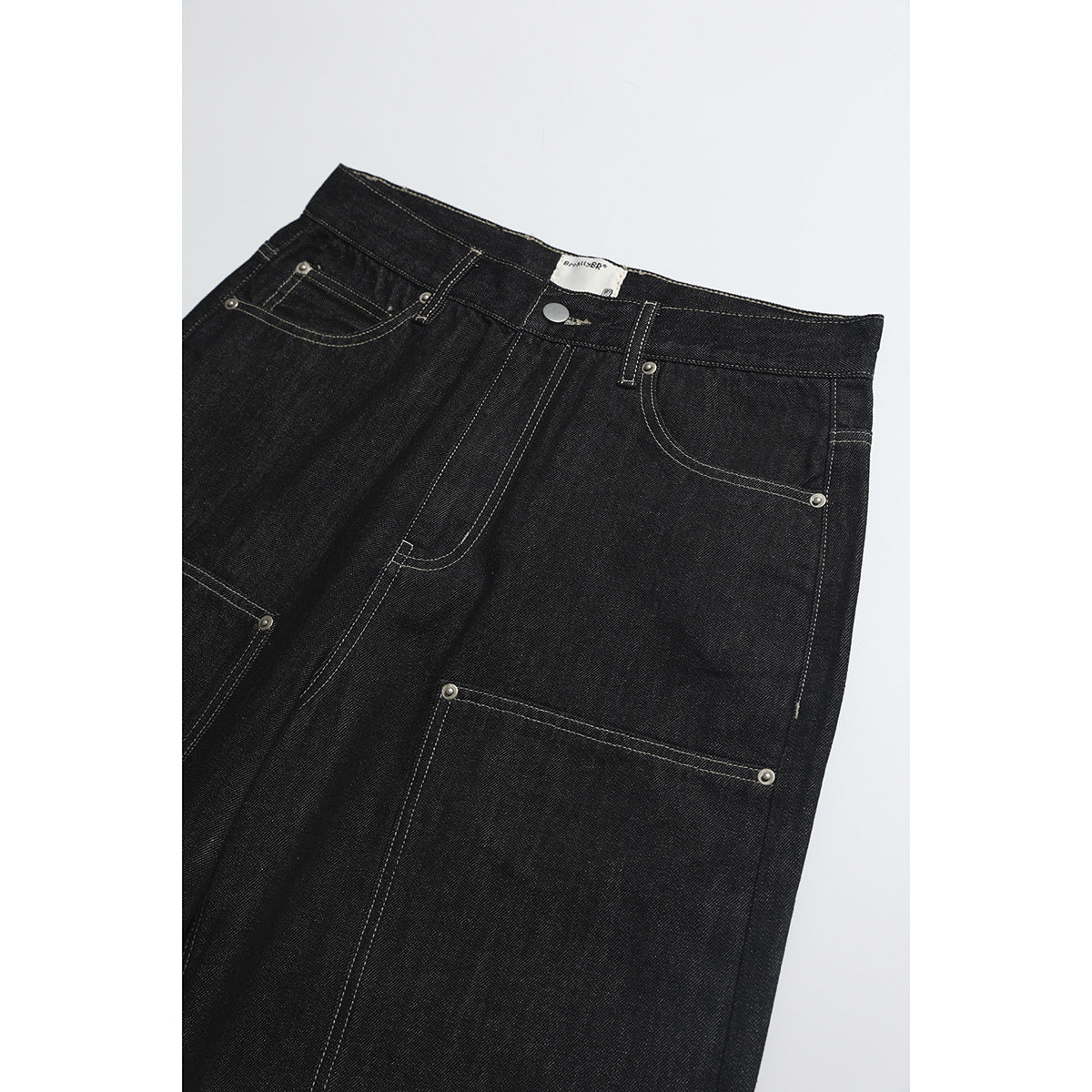 Close-up of black jeans showing the waistband, front pockets, metal rivets and large utility pocket.
