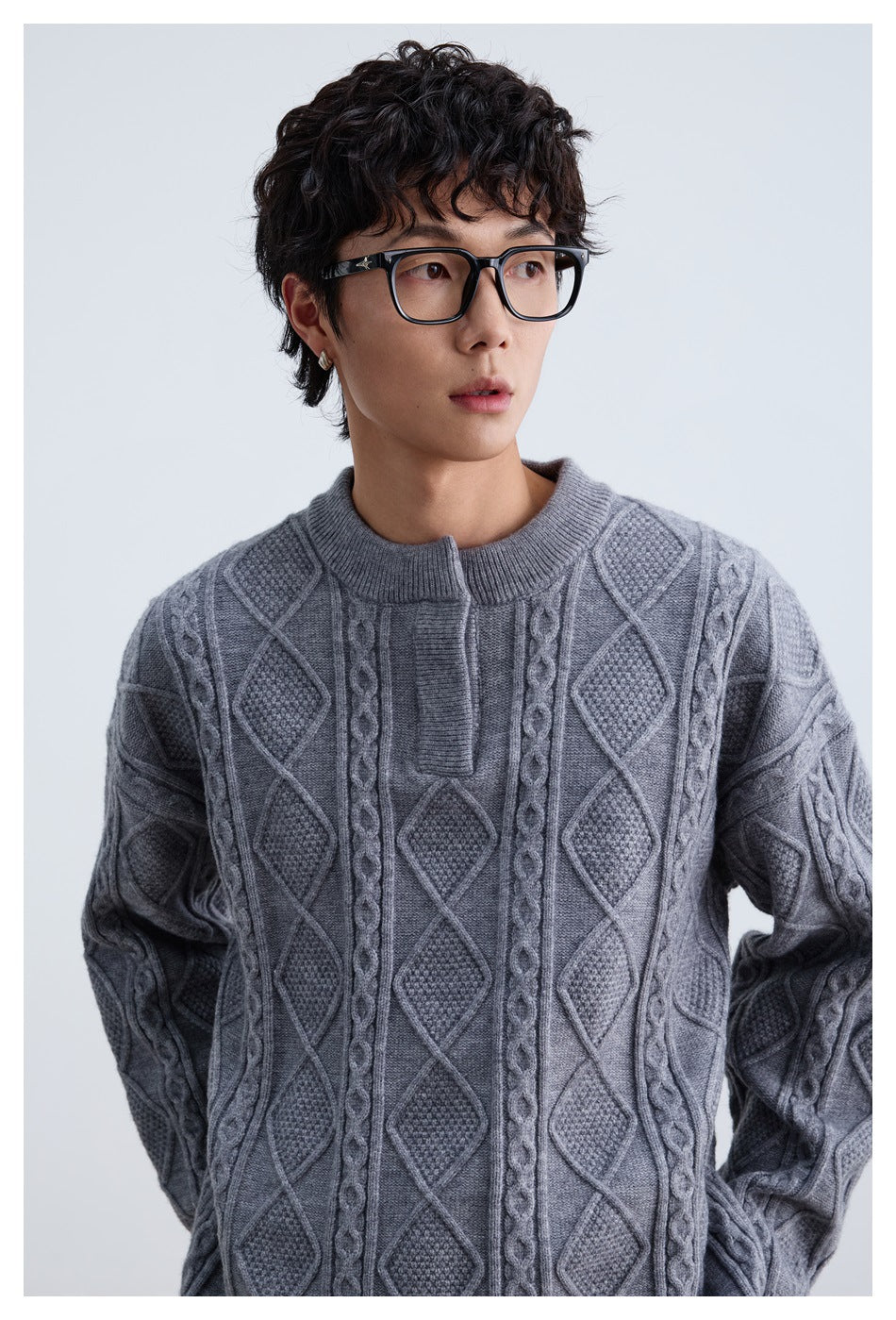 Close view of a model wearing a gray cable-knit sweater with diamond panels, braided cables, and a ribbed crew neck.