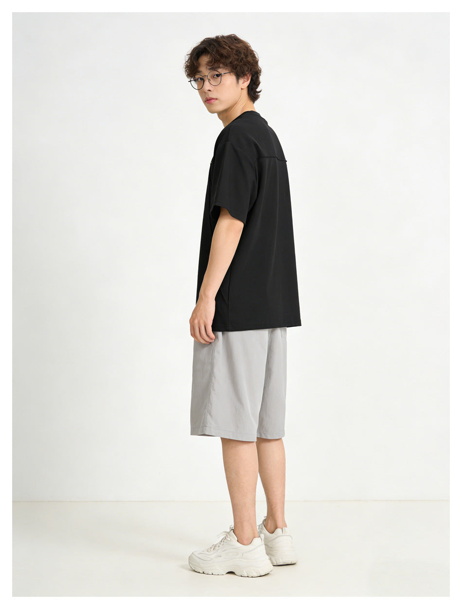 Side and rear view of a model wearing a plain black short-sleeve shirt and light gray shorts.