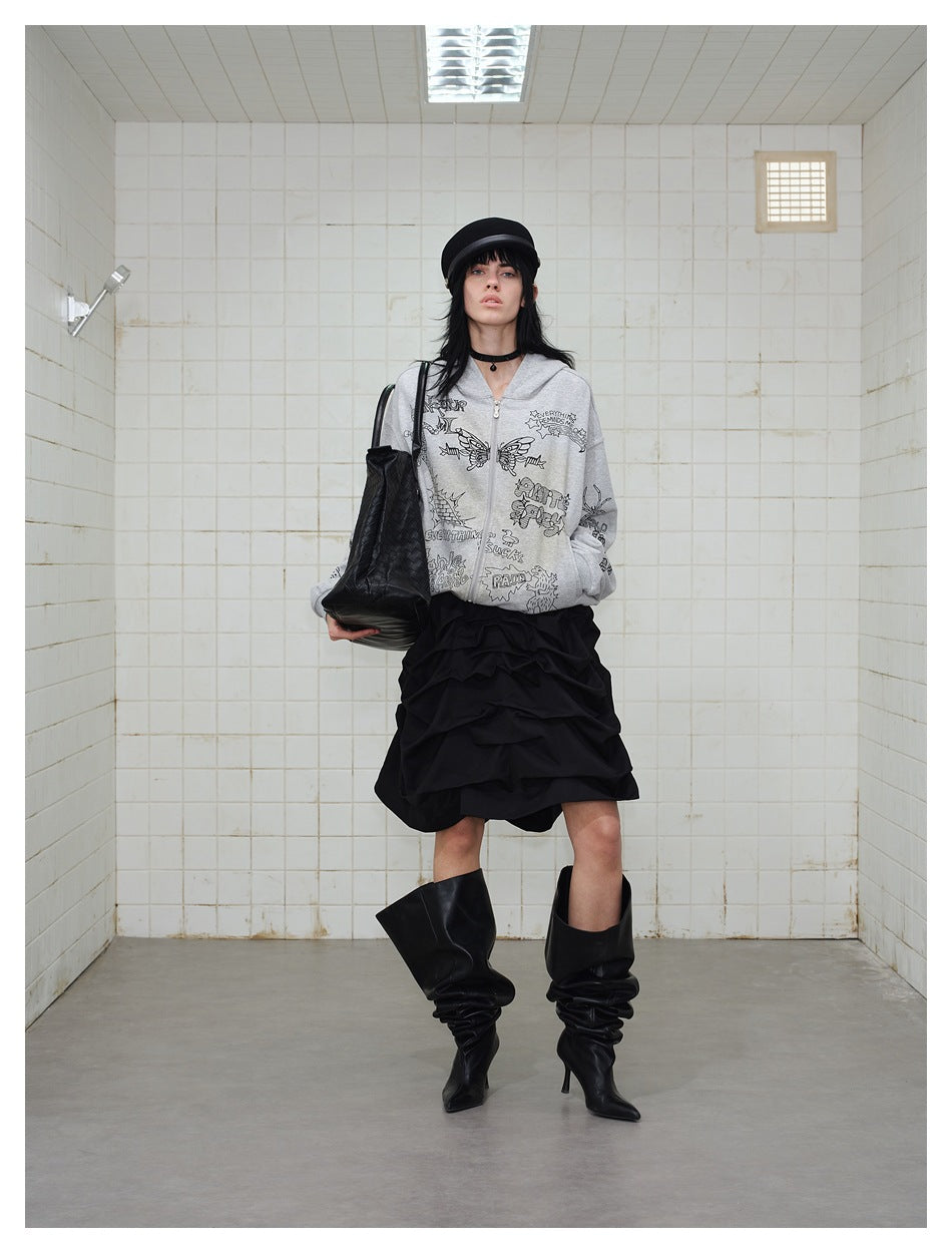 Front view of a model in a gray graphic zip-up hoodie, layered black skirt, and slouchy black boots.