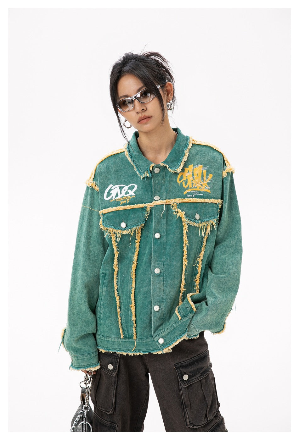 Front view of a model wearing a teal jacket with yellow frayed trim, chest graphics, and flap pockets.