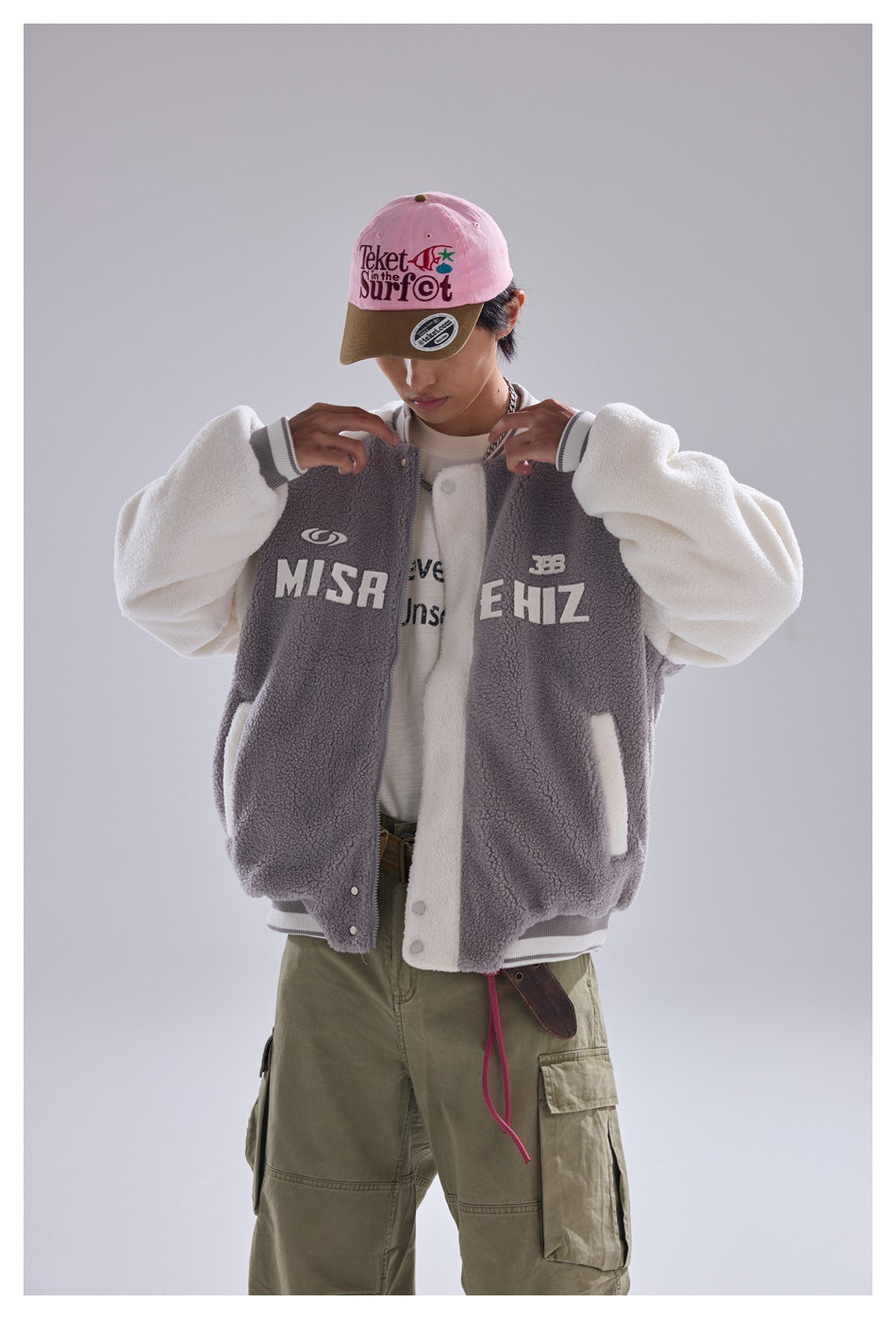 Close front view of a model wearing a gray-and-white fleece varsity jacket with large chest lettering and snap buttons.