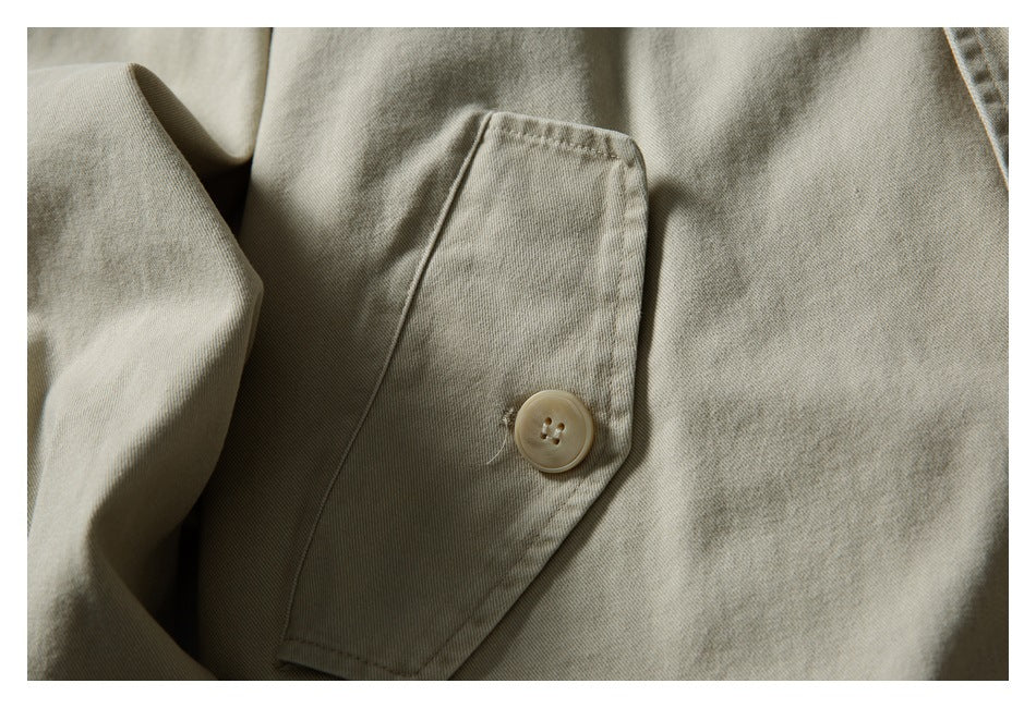 Close-up of a light beige jacket's rectangular pocket and round four-hole button.