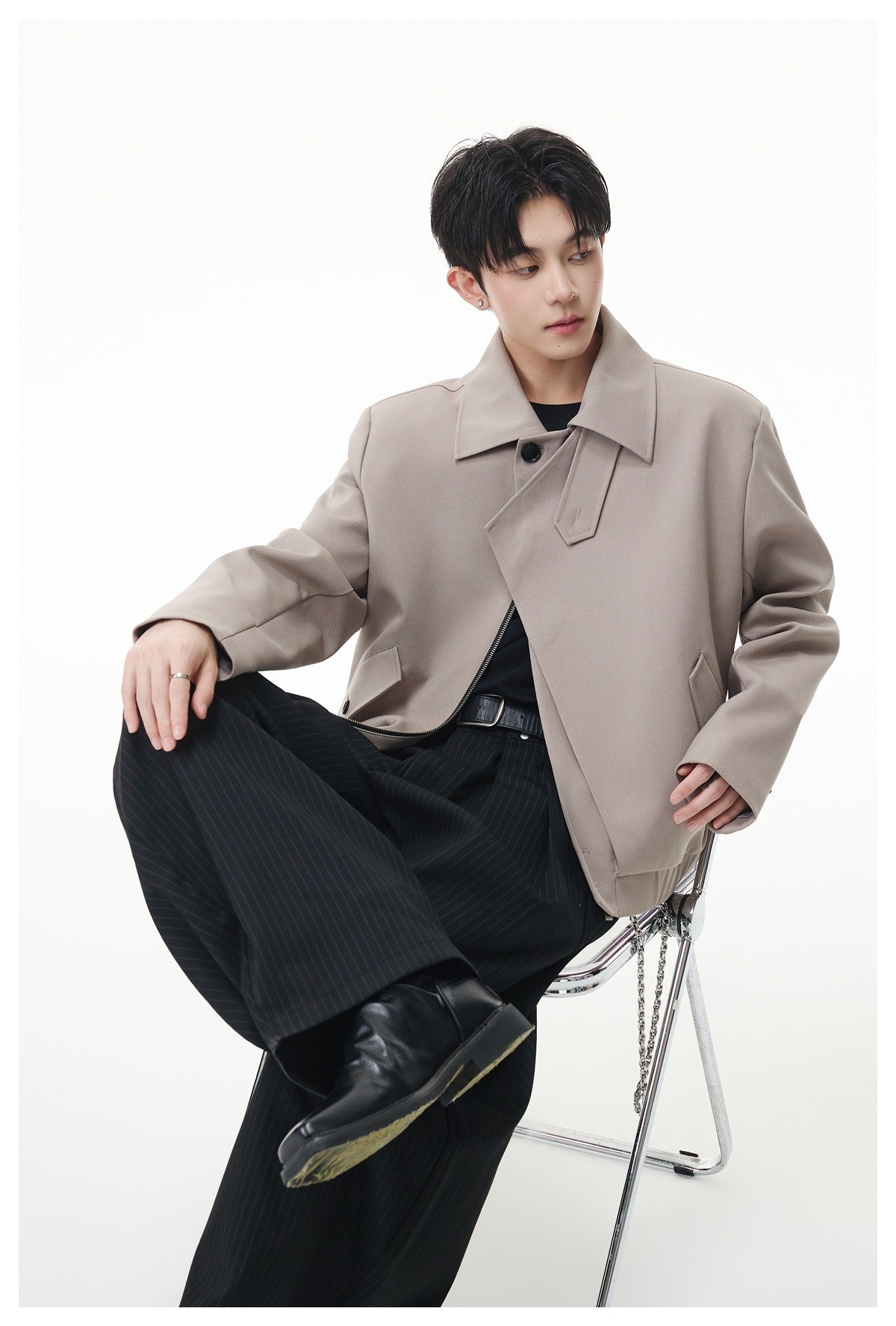 Model seated on a chrome chair wearing a light gray cropped jacket with black pinstripe wide-leg pants