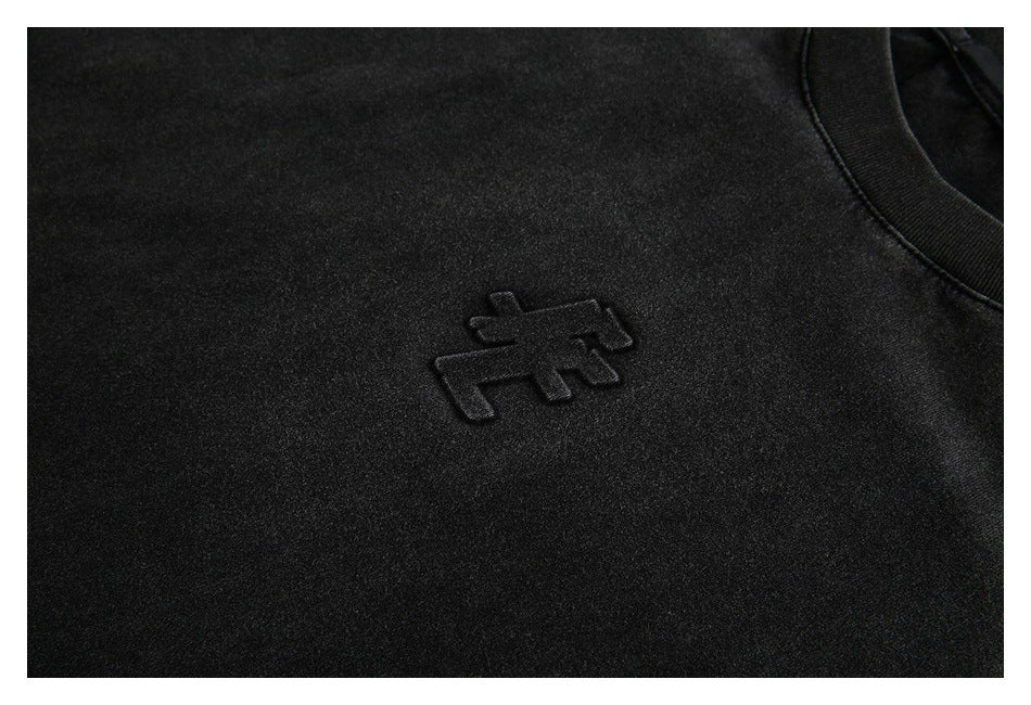 Close-up of a raised black emblem on the chest of a black shirt.