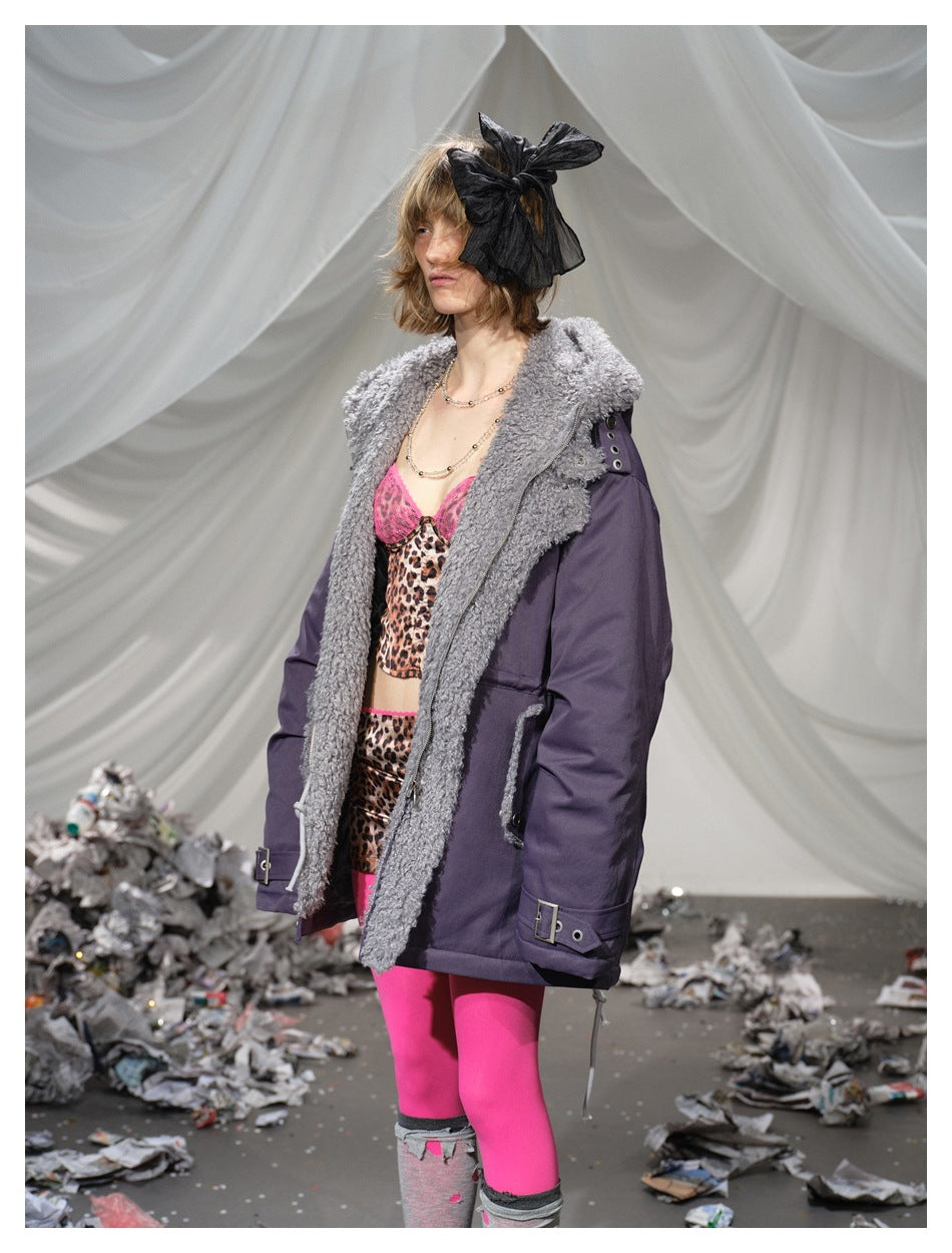 Three-quarter view of a model in a plum parka with a large gray collar, side pockets, and cuff buckles.